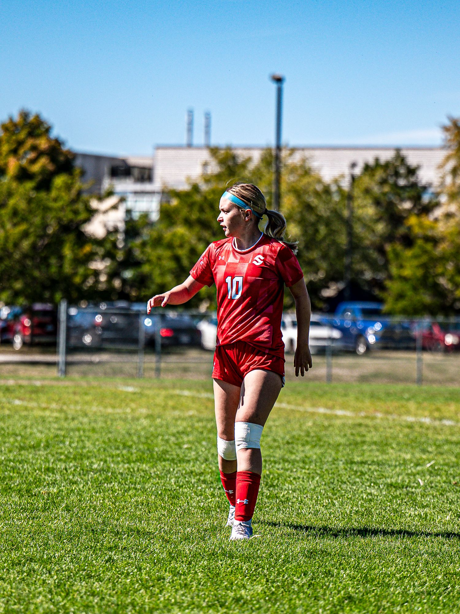 Soccer player in red jersey runs across green grass field during daytime.