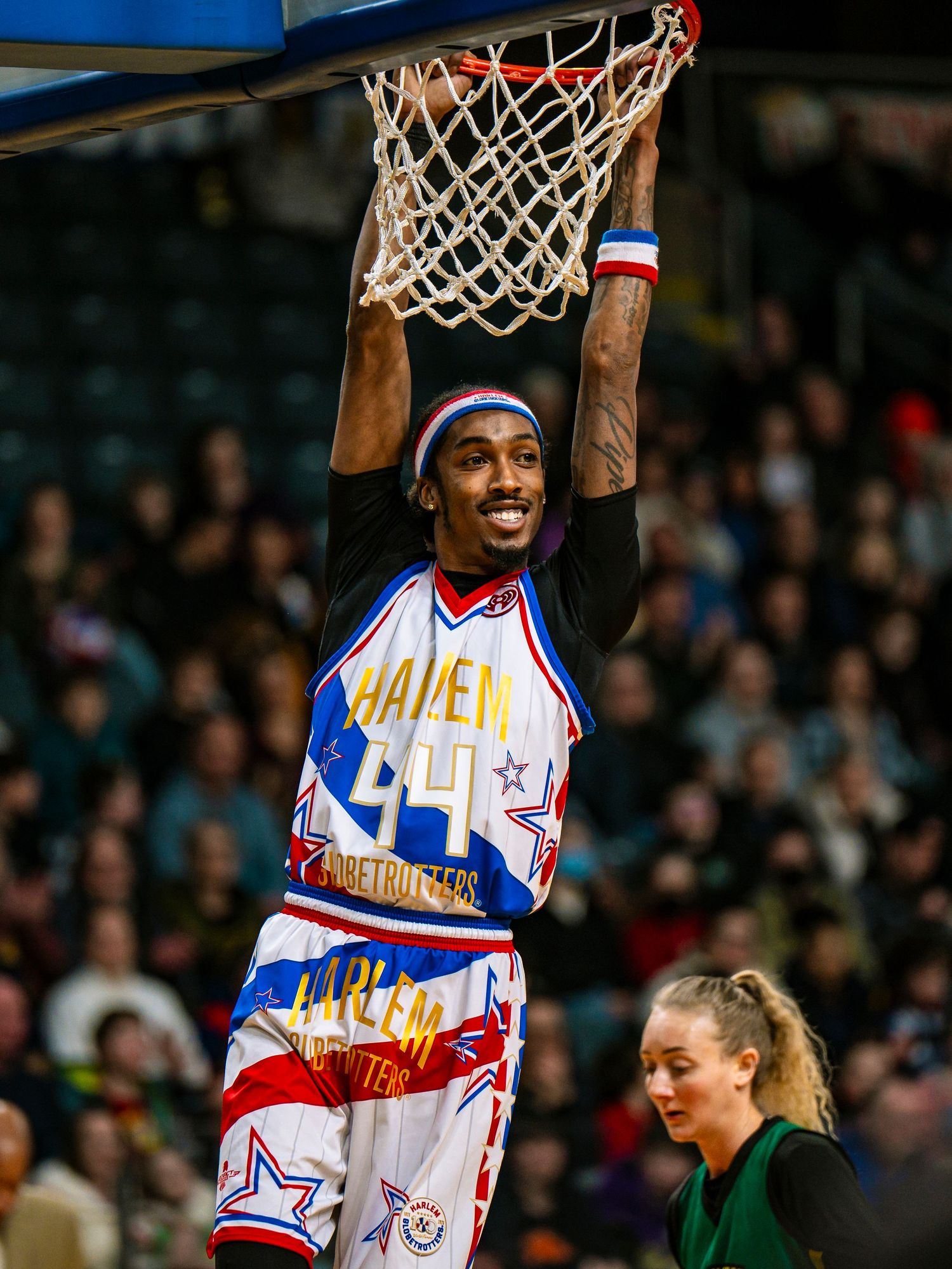Harlem Globetrotters basketball player performs acrobatic slam dunk during exhibition game.