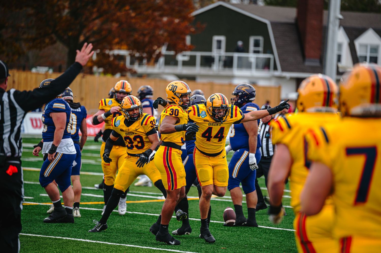 Football players in yellow uniforms celebrate on field during a competitive game on a green turf field.