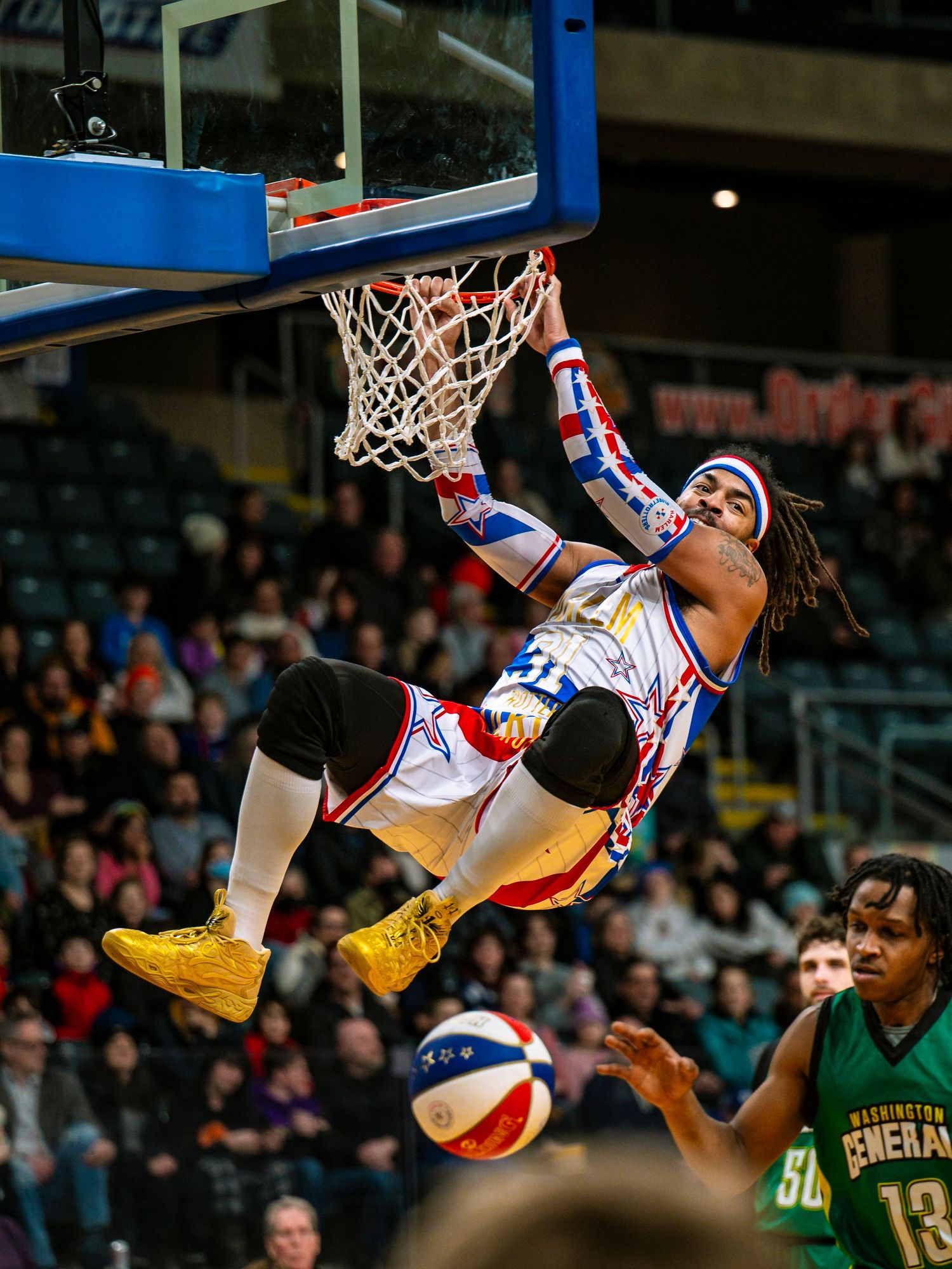 Basketball performer hangs upside down from hoop during Harlem Globetrotters show.