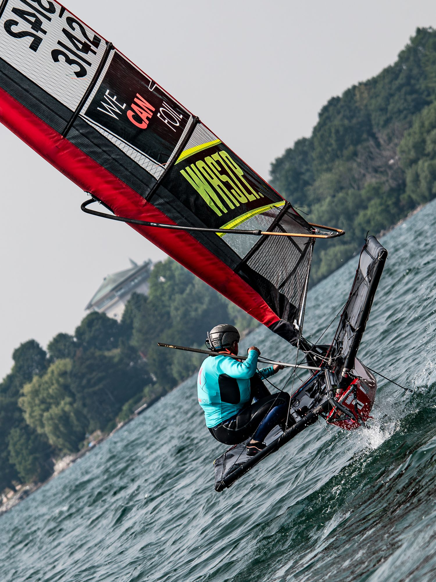 A windsurfer glides across choppy waters near a mountainous coastline, showcasing dynamic action in turquoise waters.