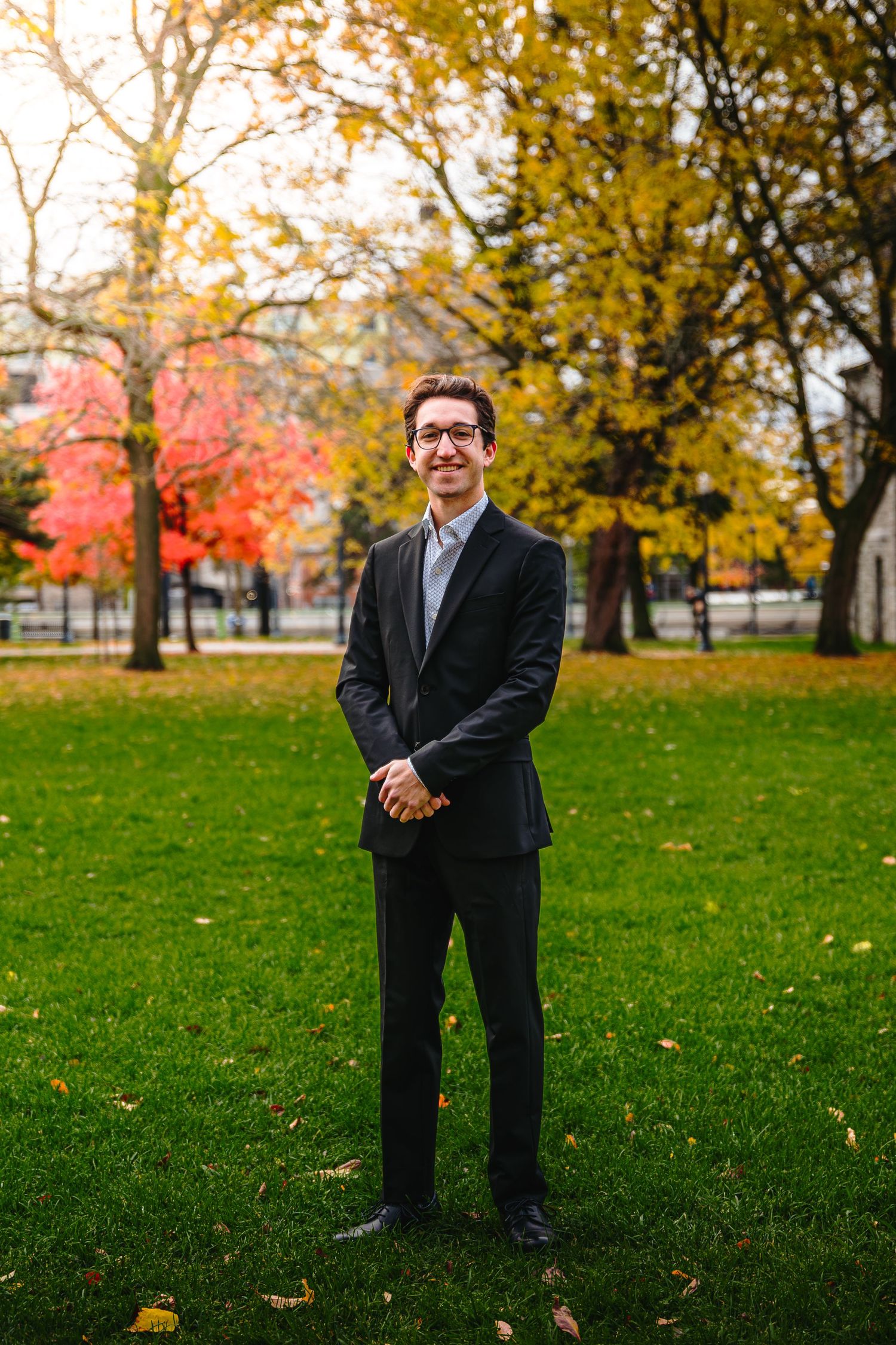 Professional portrait on green lawn with autumn trees and red foliage in background during fall season.