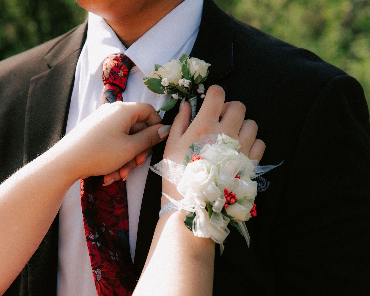 Someone adjusts a white floral boutonniere on a black suit jacket with a red tie.