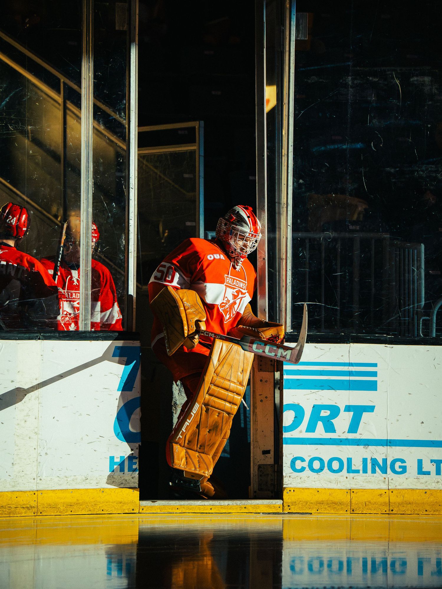 Hockey goalie in orange jersey standing in front of the net during a game.