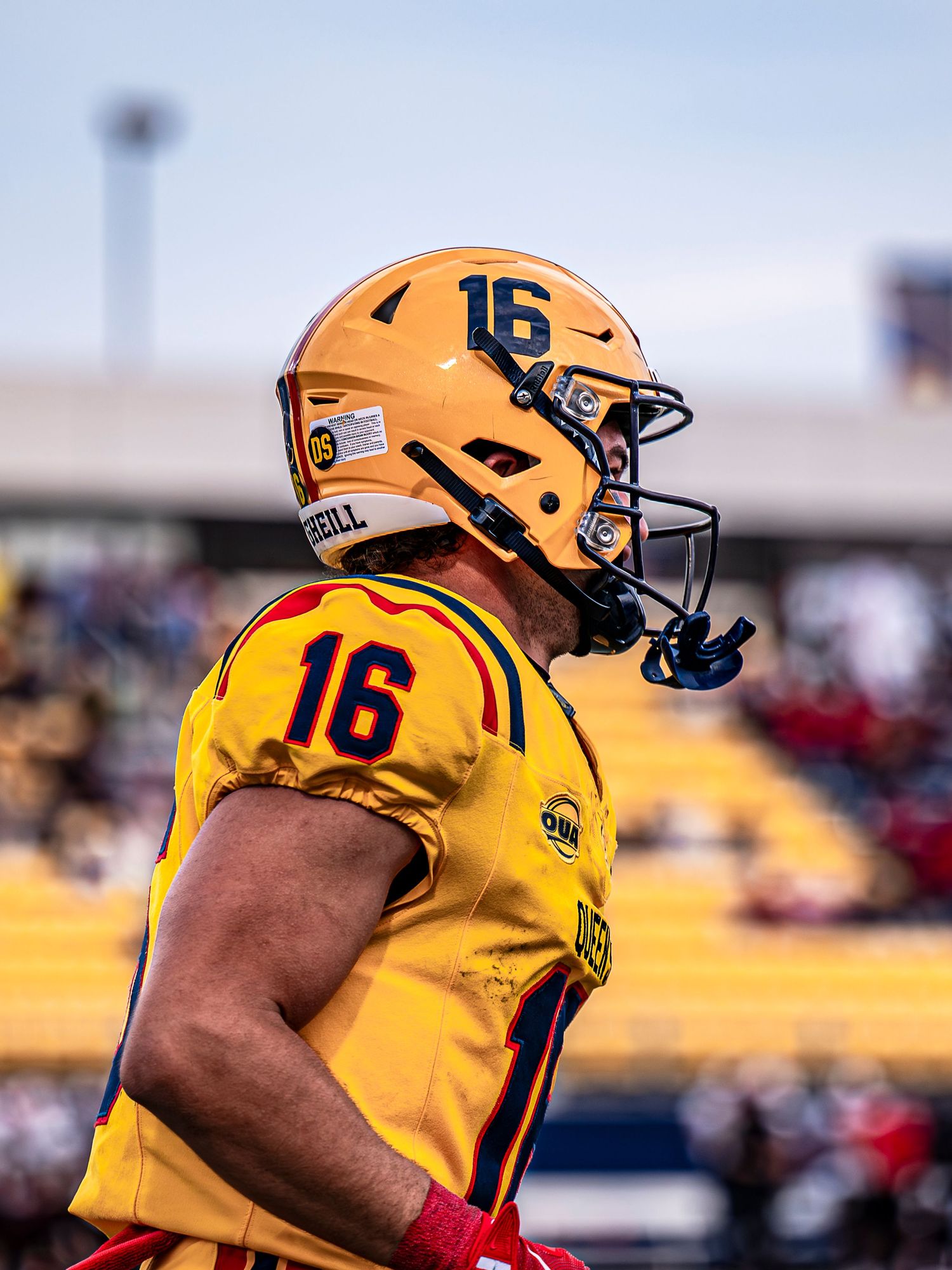 Football player in yellow jersey number 16 wearing helmet stands on field during game.
