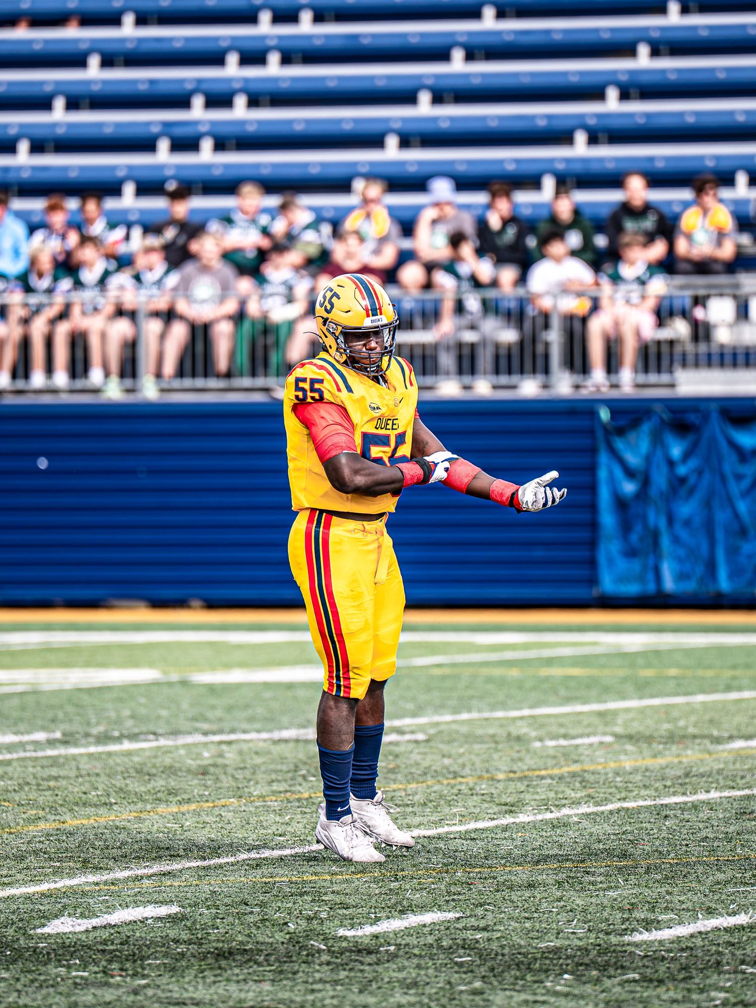 Football player in yellow and black uniform practices punting drills on a turf field with stadium seating visible.