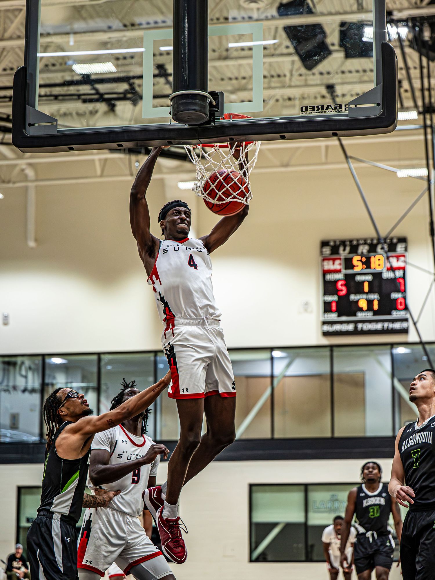Basketball players in white jerseys leap for a slam dunk during an indoor game.