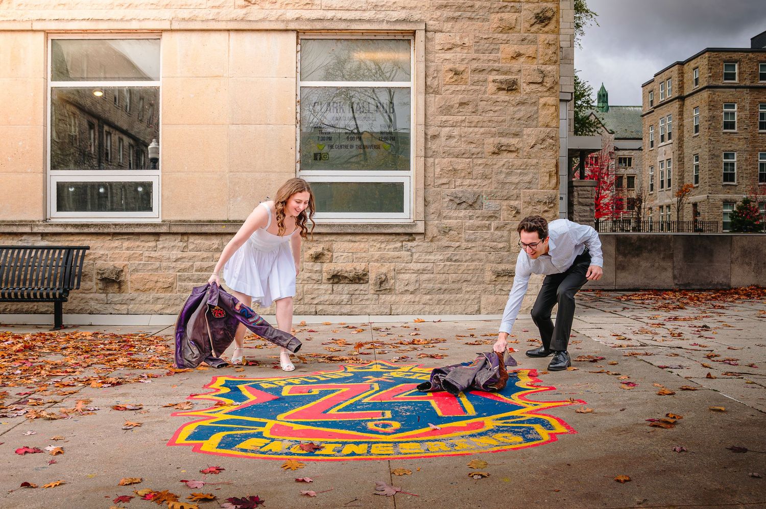 A person arranges colorful geometric shapes in a circular pattern on an outdoor concrete surface during autumn.