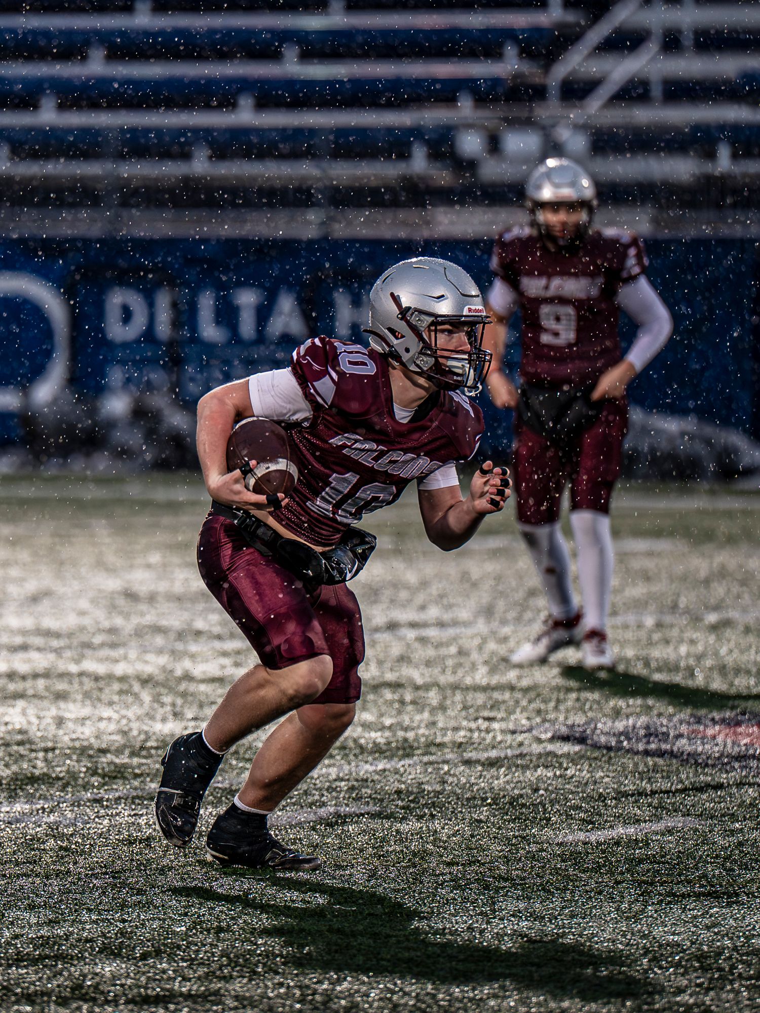 Football player in maroon uniform performs diving motion sequence on wet field during game.