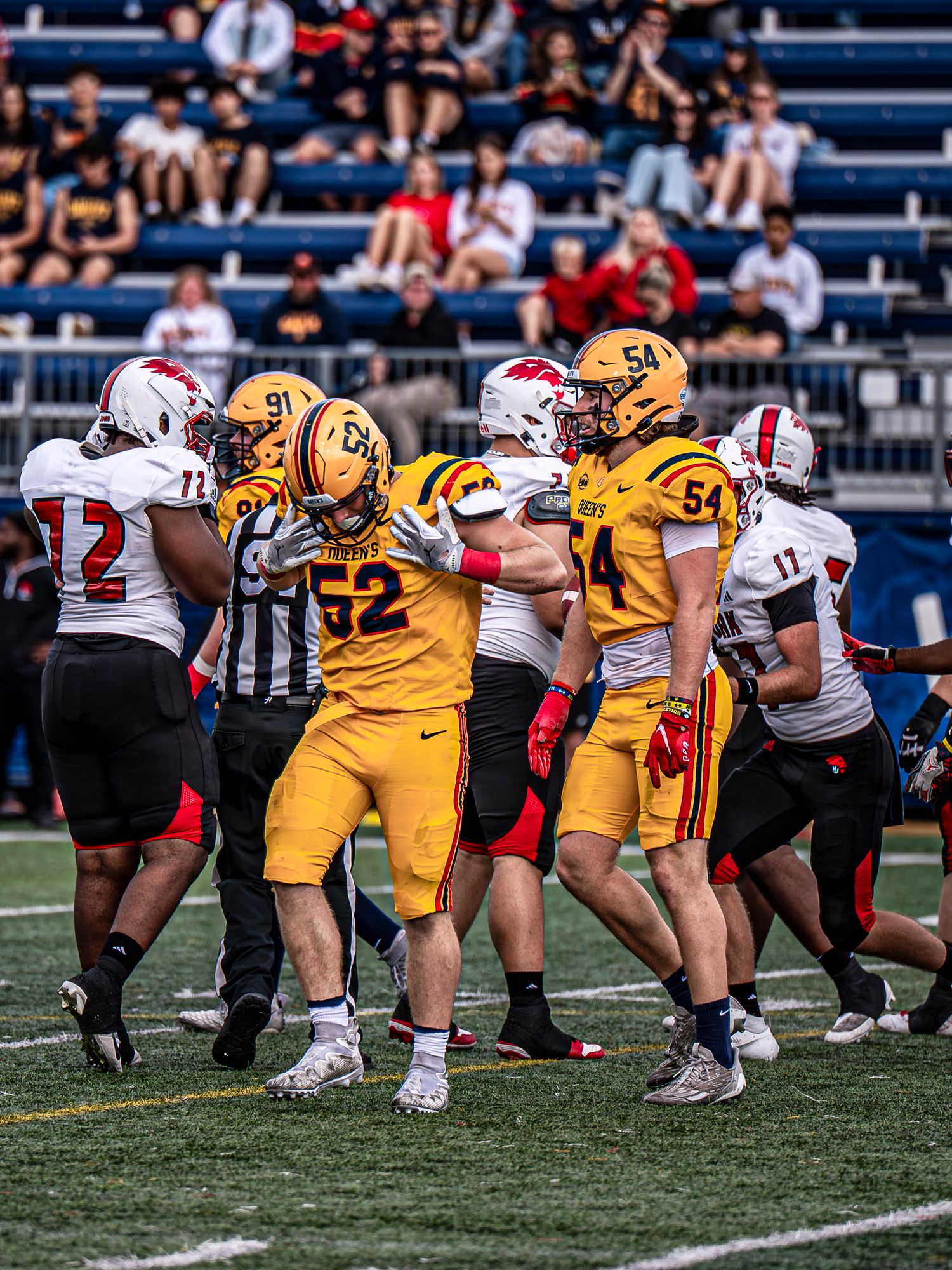 Football players in yellow and white uniforms face off during game with referee present.
