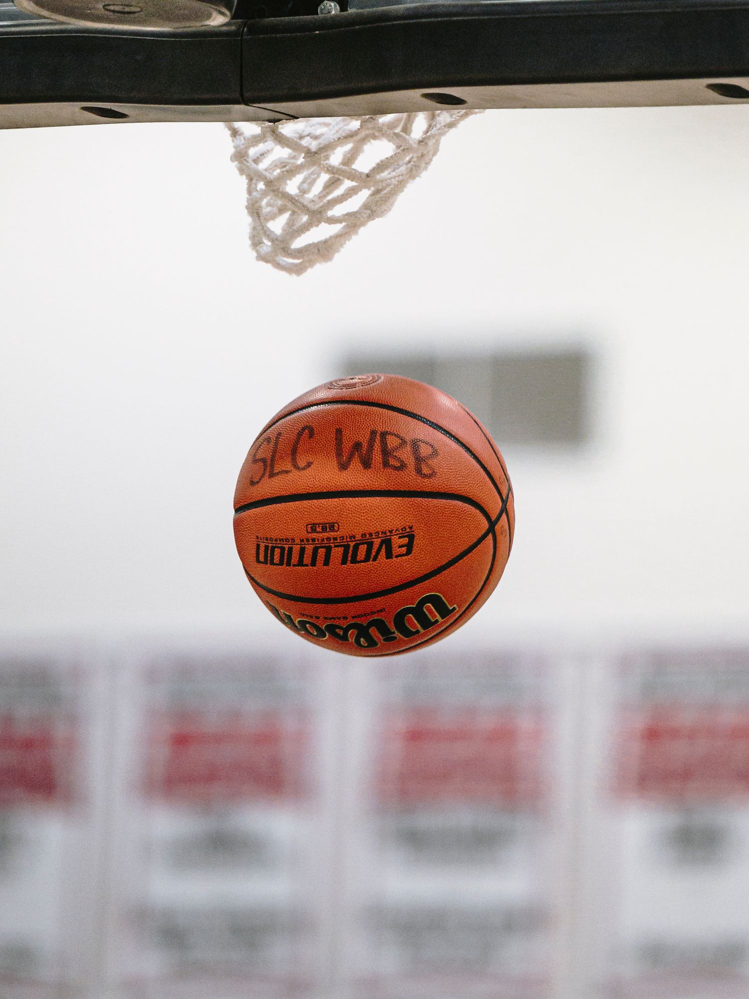 Wilson Evolution basketball labeled SLC WBB passing through a net during a women's basketball game.