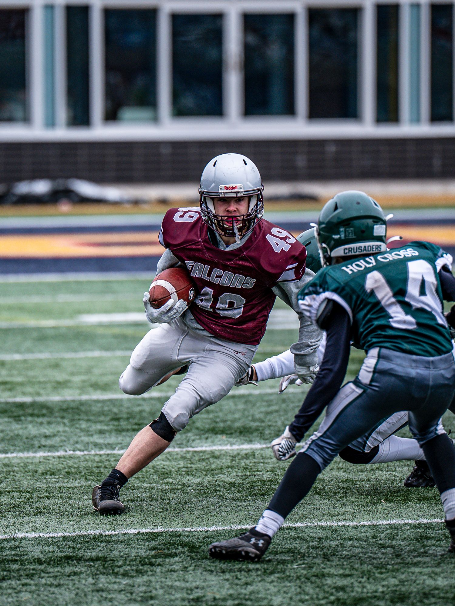 Football player in maroon jersey evades tackle from defender in green uniform.