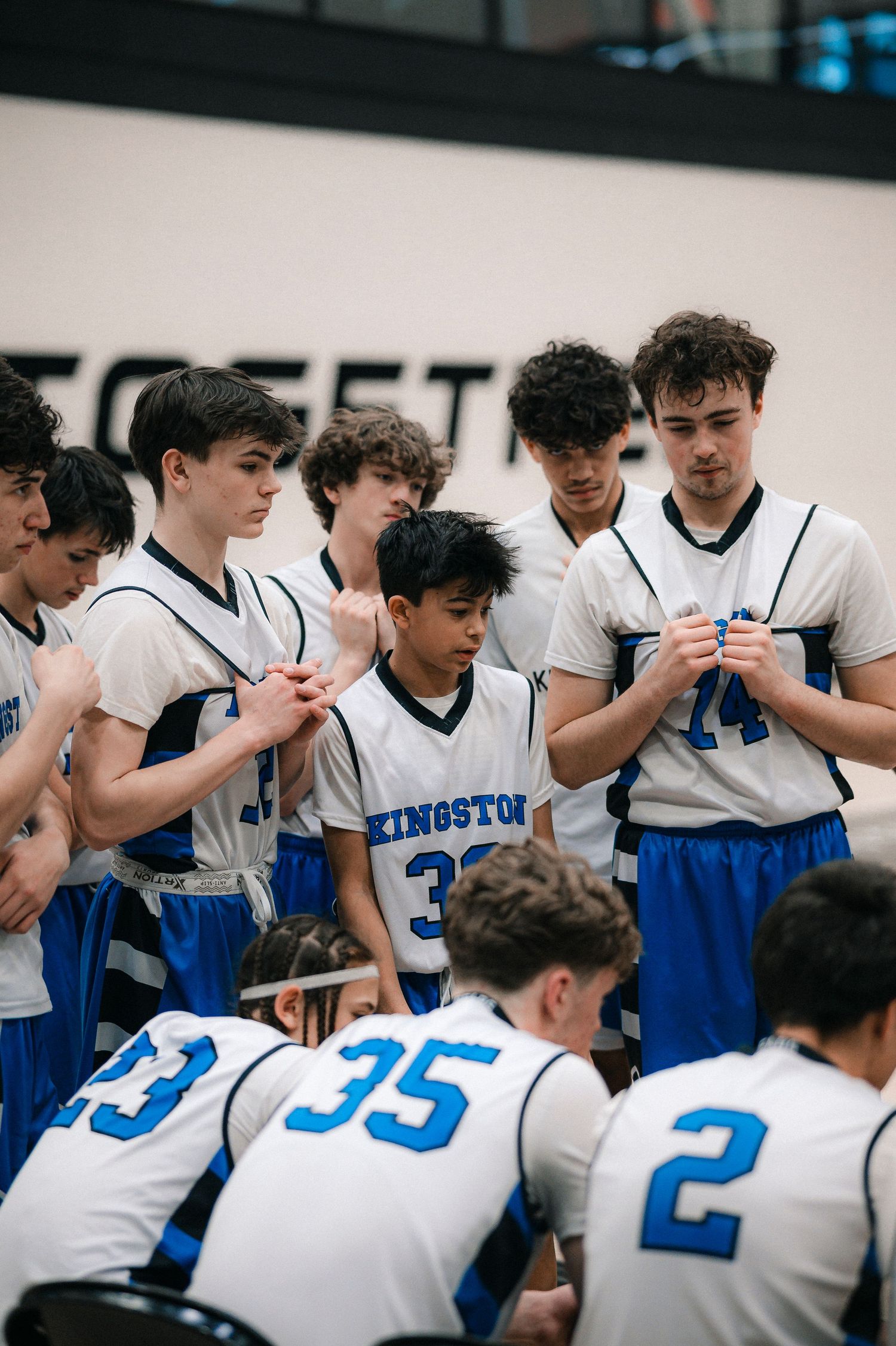 Kingston youth basketball team huddles together in white and blue uniforms during a game timeout.