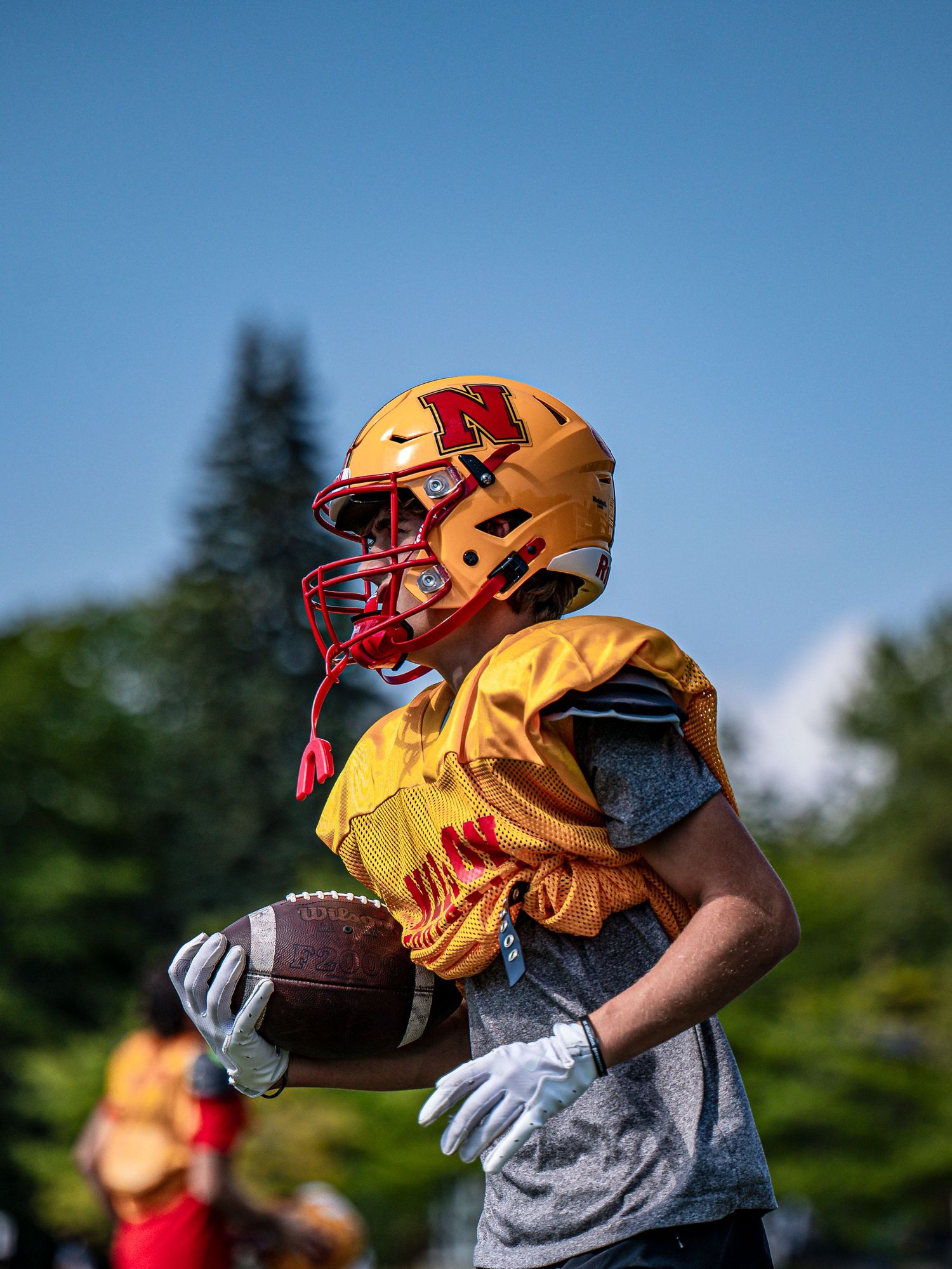 Close-up of football player's hands holding a brown football against blue sky background.