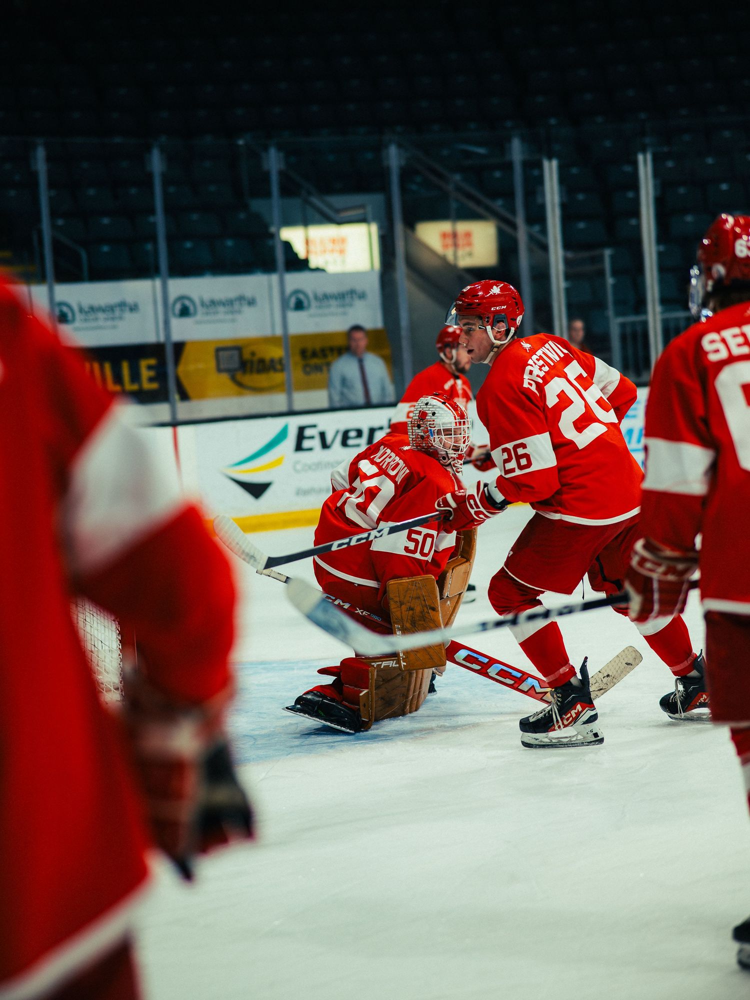 Hockey players in red jerseys stretch on the ice during a pre-game warmup routine at an indoor arena.