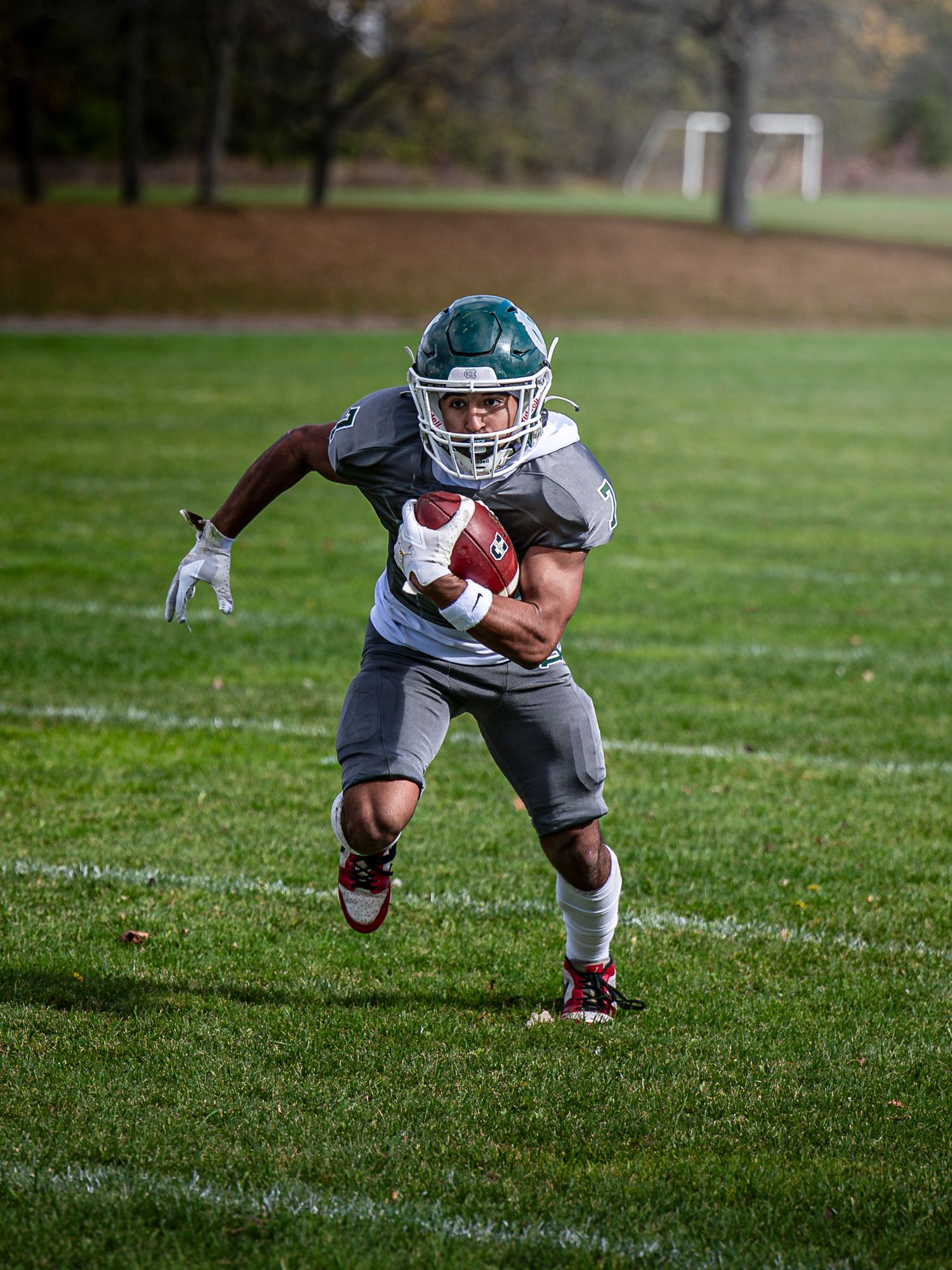 Football player in gray uniform demonstrates diving catch progression on grass field.