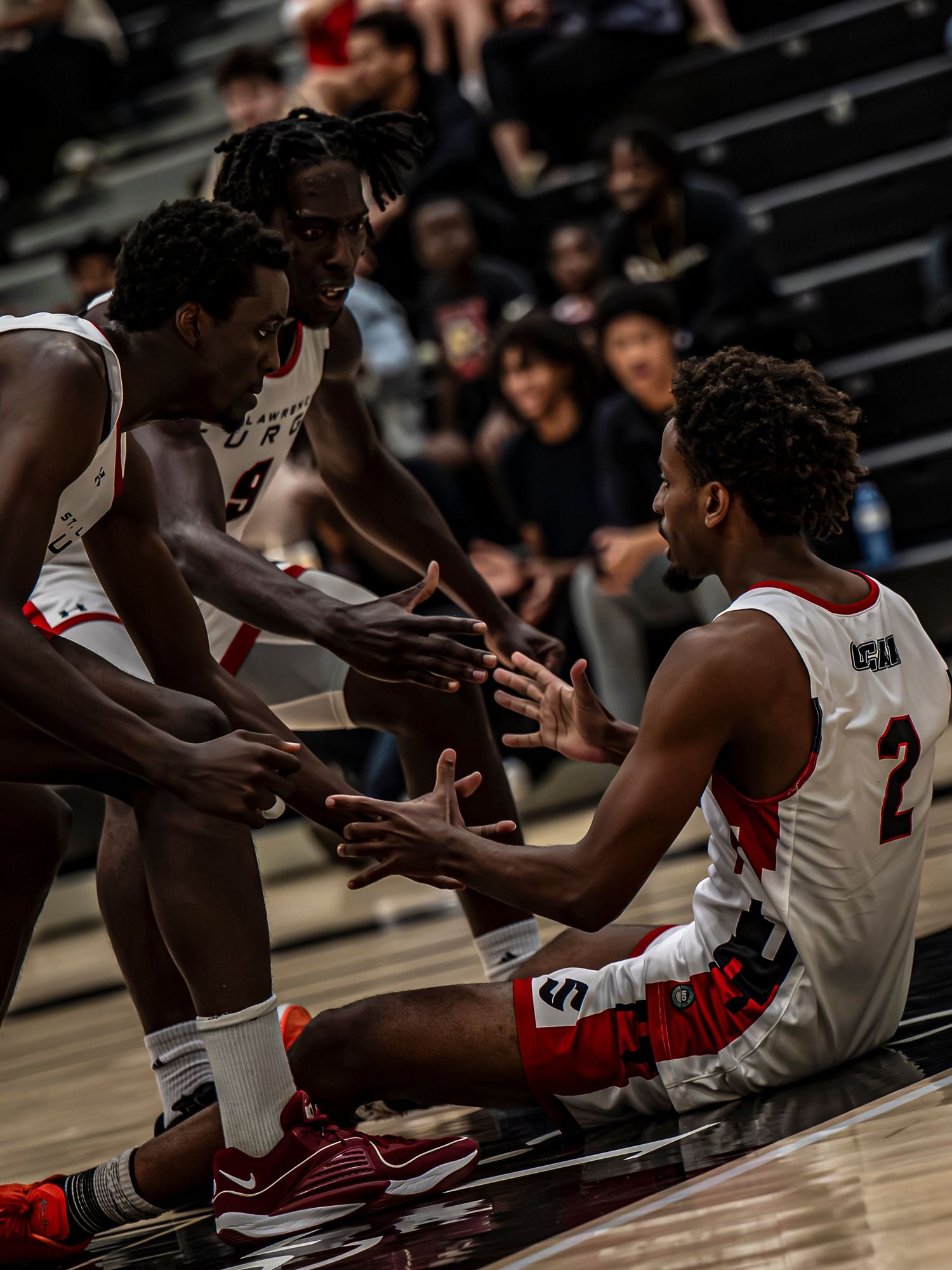Basketball players sit on the sideline during a game wearing red and white uniforms.