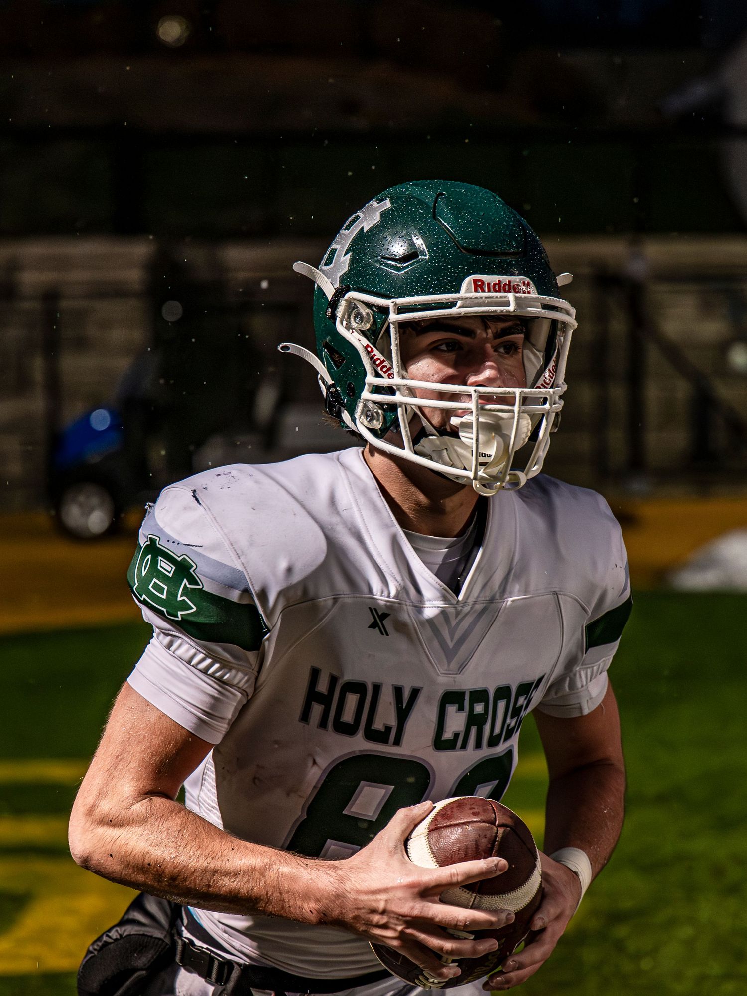 Football player in white Holy Cross uniform carries ball during night game.