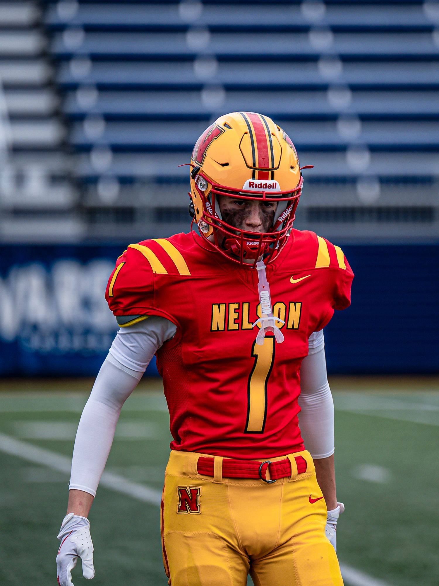 Football player in red and yellow Nelson uniform stands ready on the field.