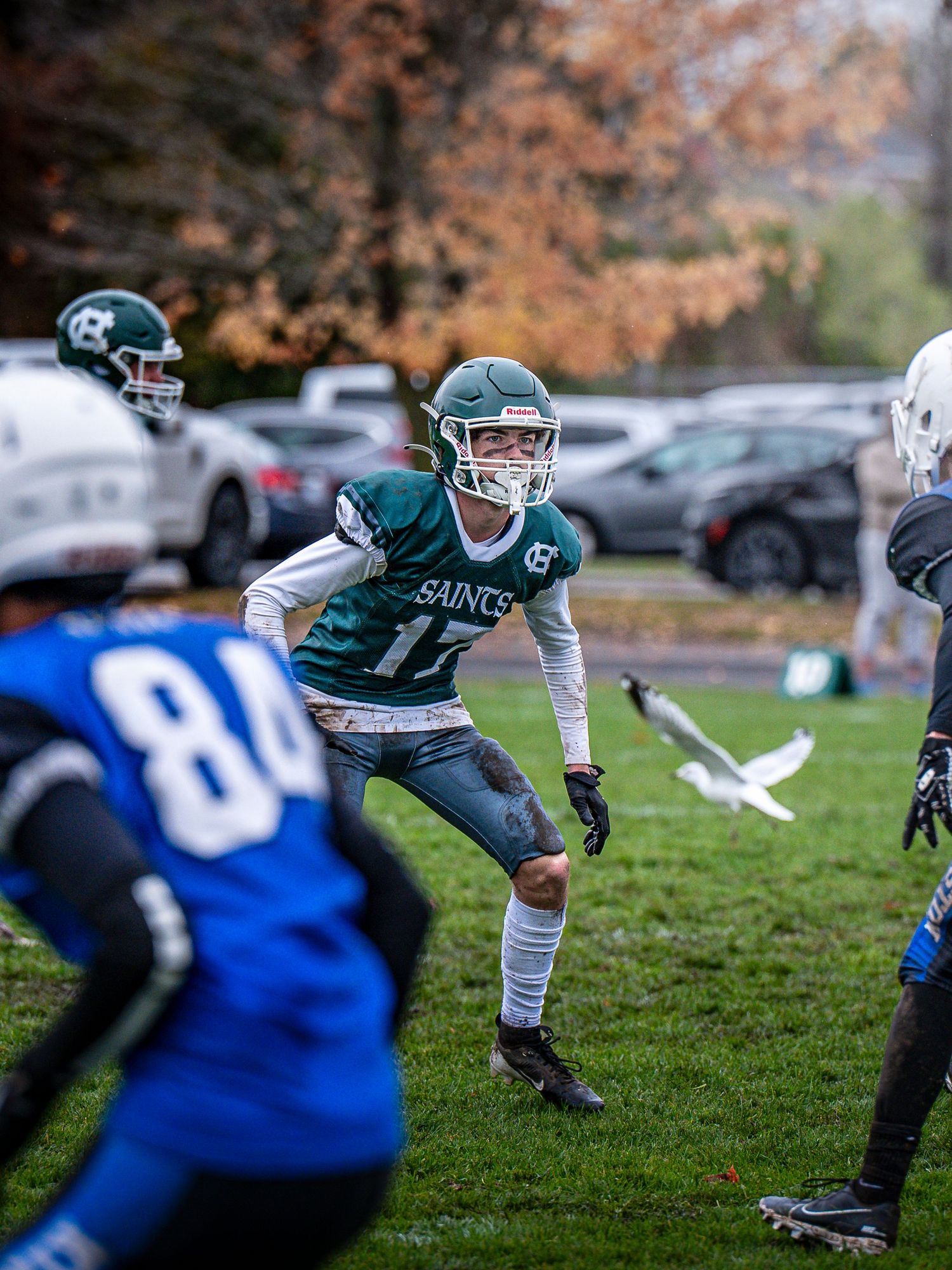 Football players in green and blue uniforms compete during fall game sequence.