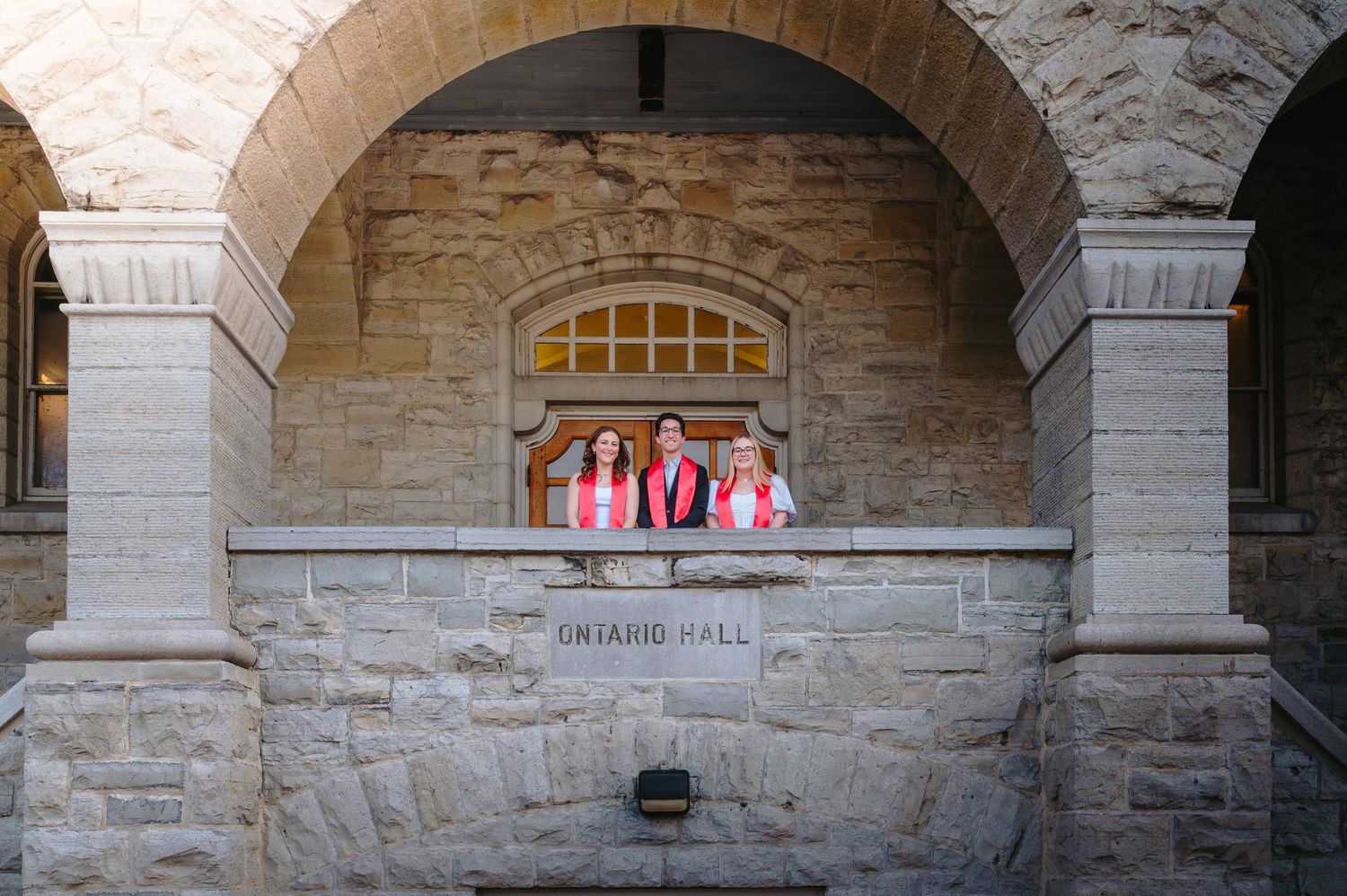 Pink and red banners displayed in an arched stone alcove at Sather Hall with classical architectural details.