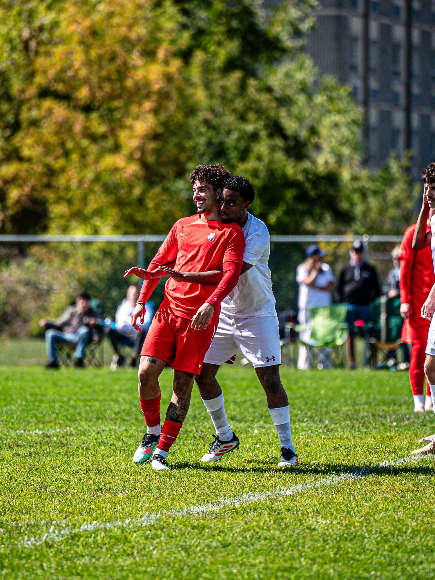 Soccer players in red and white jerseys battle for possession on a sunny grass field.