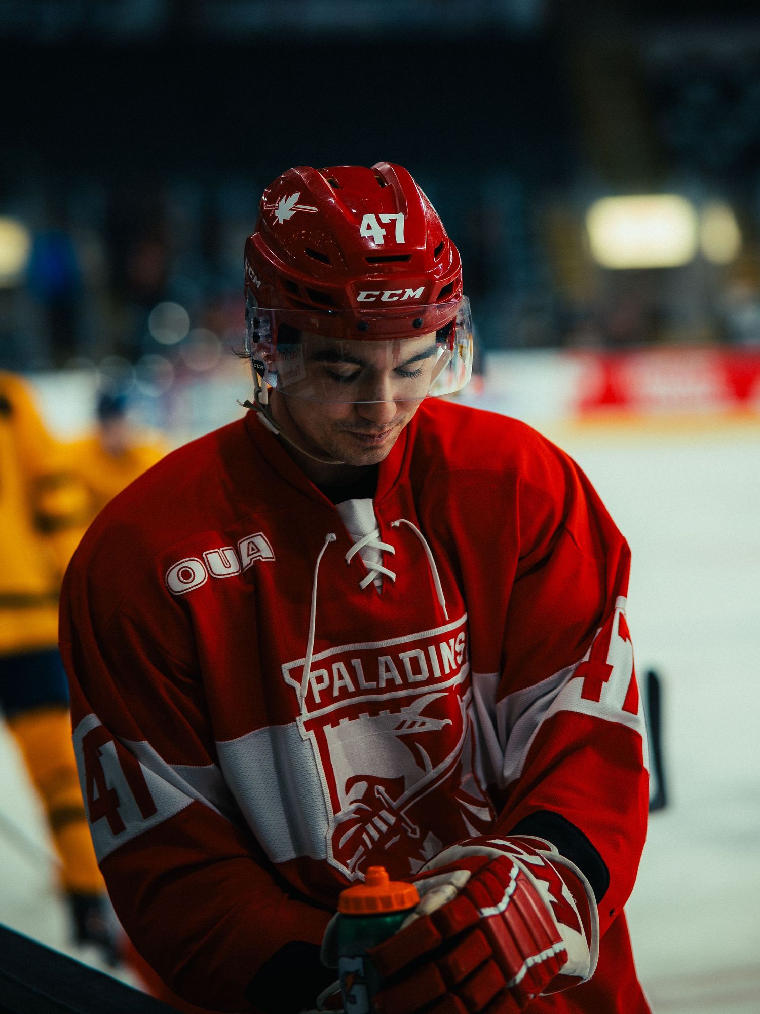 Hockey player in red jersey and white gloves skates on ice during competitive match.