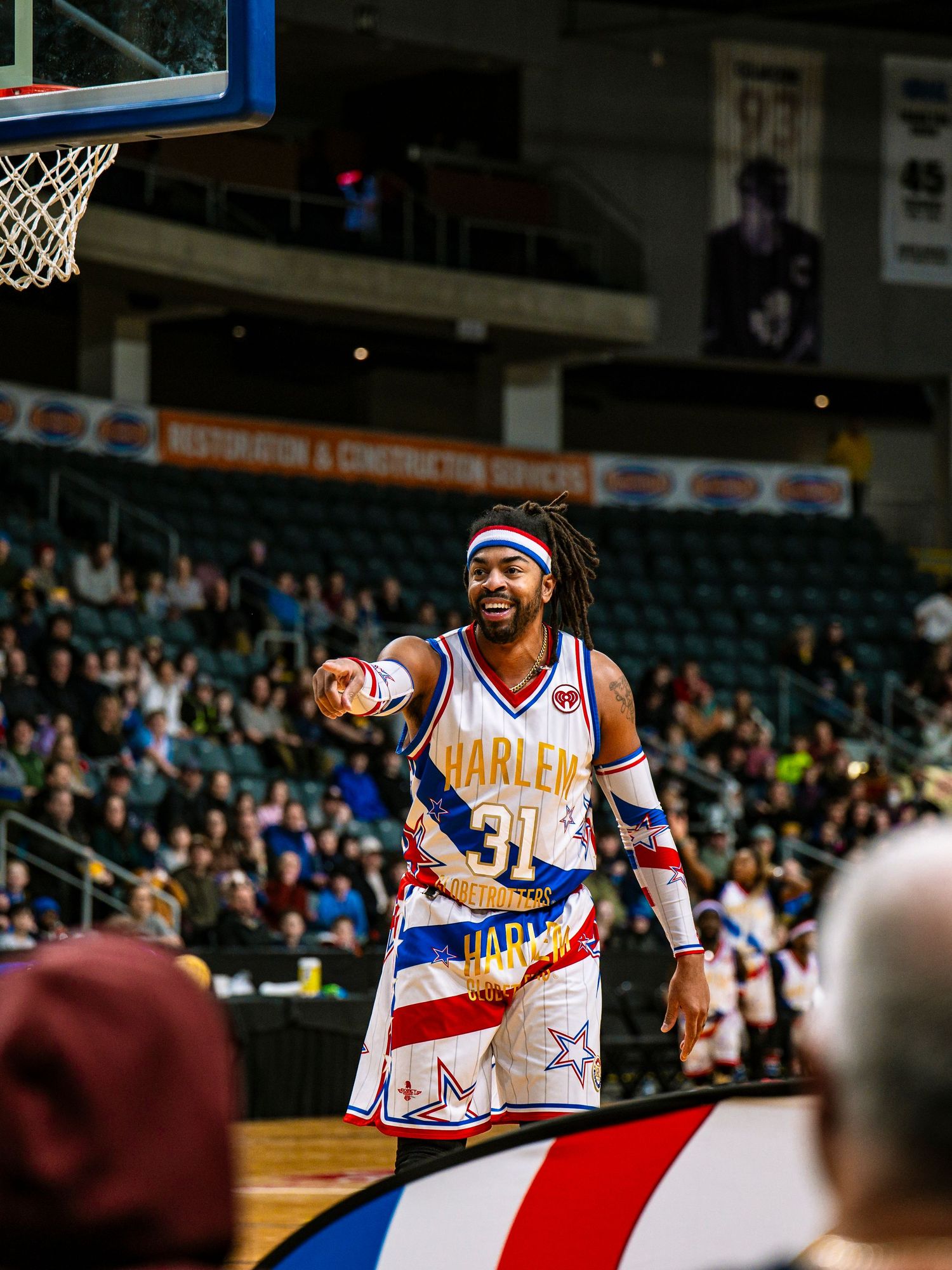 Basketball player in Harlem Globetrotters uniform points and gestures during game performance at indoor arena.