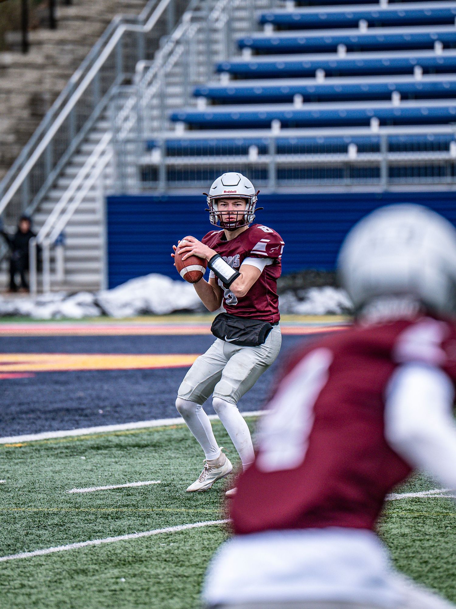 A football player in maroon uniform catches a pass on the field with empty bleachers in background.