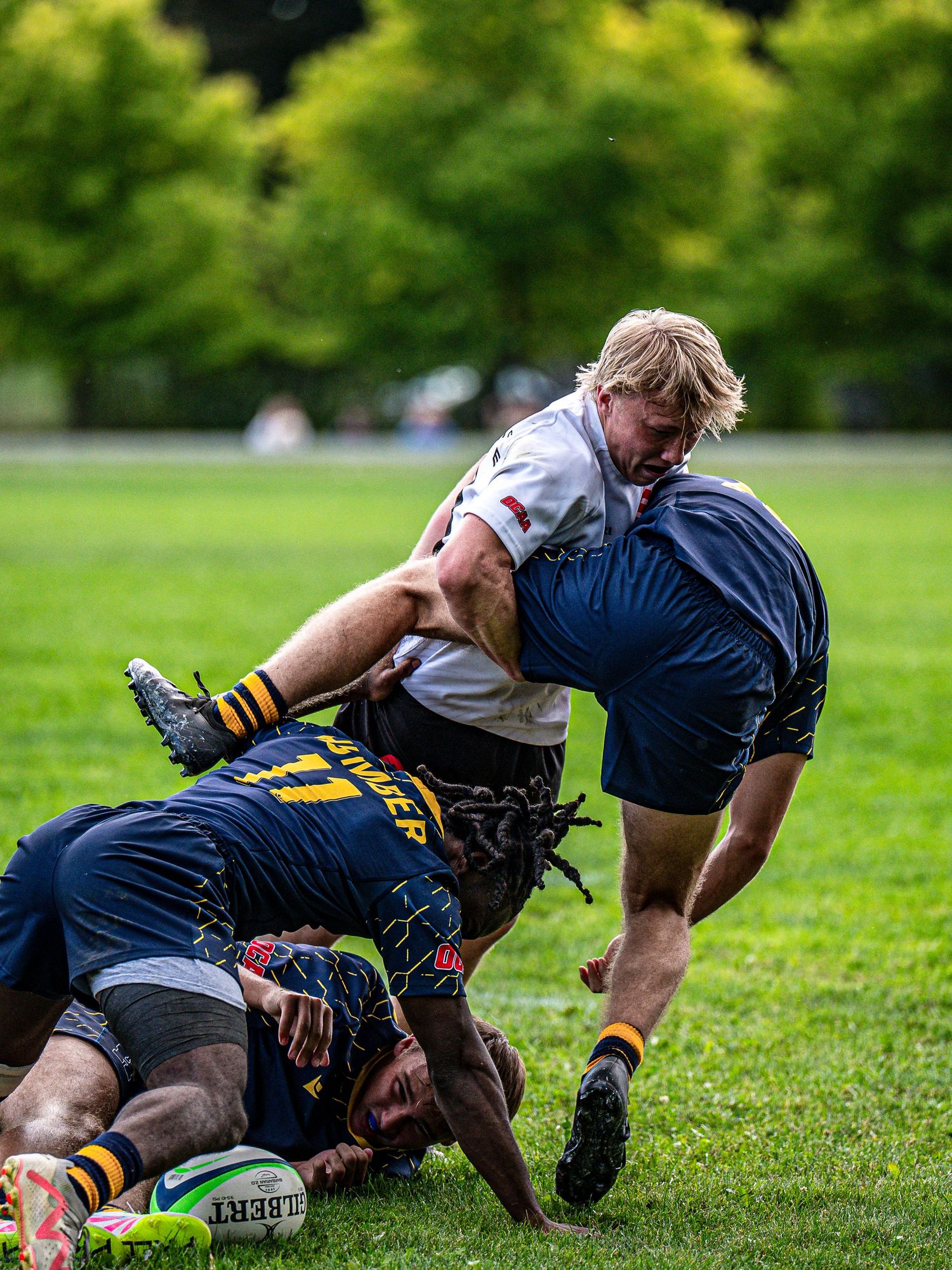 Rugby players engage in physical tackle during intense match on grass field.