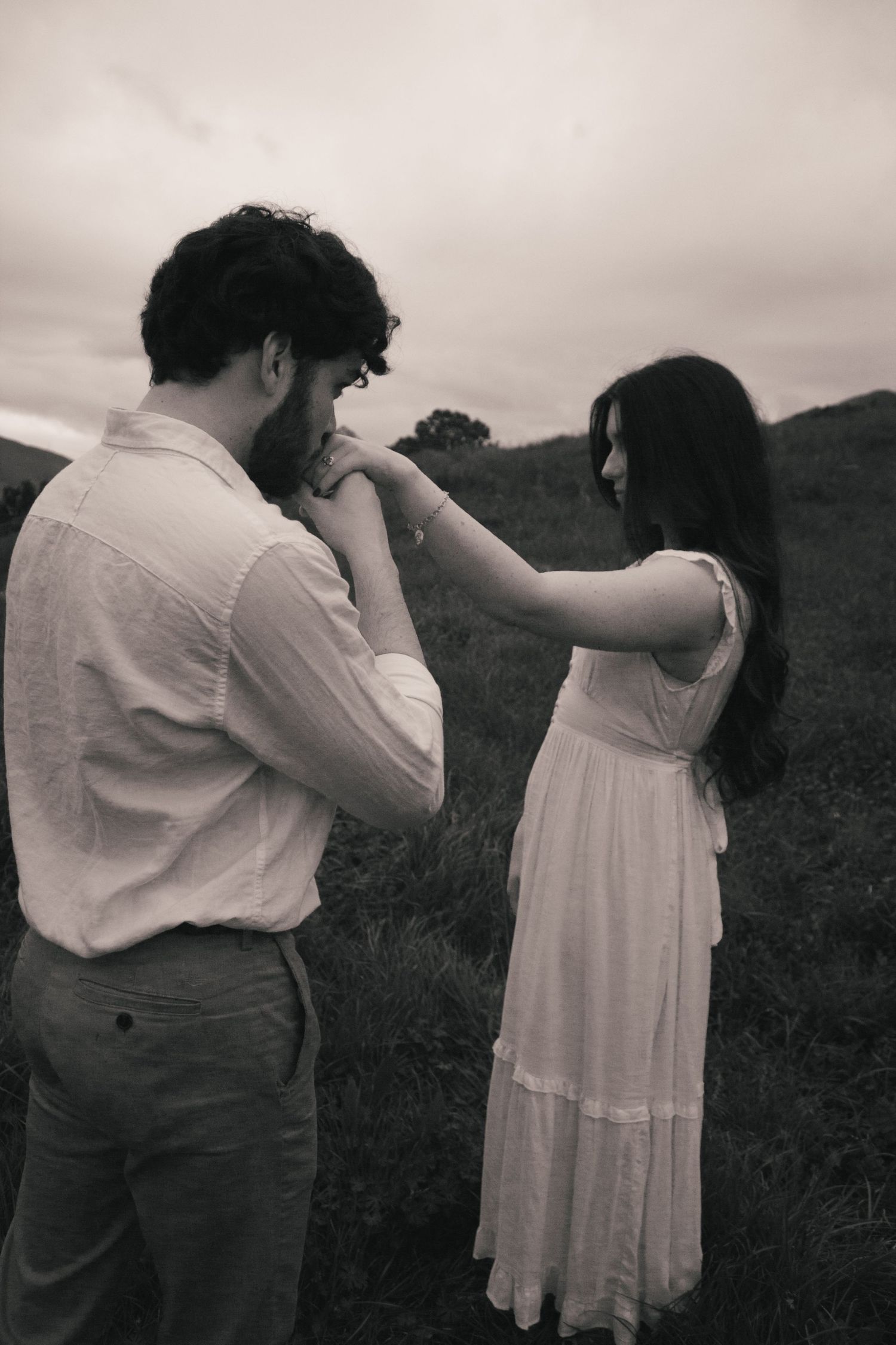 A romantic black and white photograph of a couple in a field, with the man gently kissing the woman's hand.
