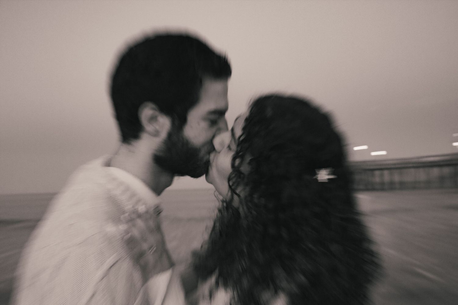 A romantic couple sharing an intimate moment at sunset on a pier in black and white.