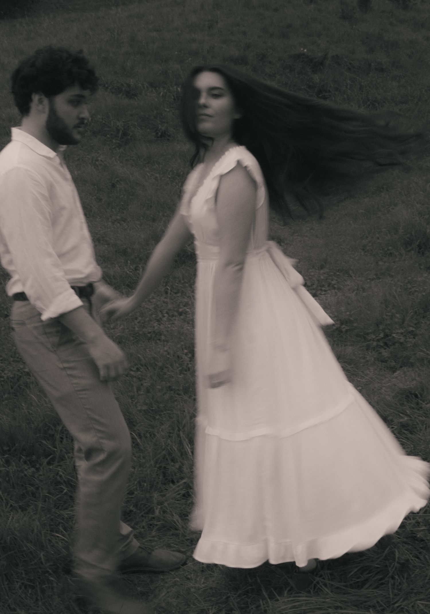 Two children in white and tan clothing dance together on grass in a vintage black and white photograph.