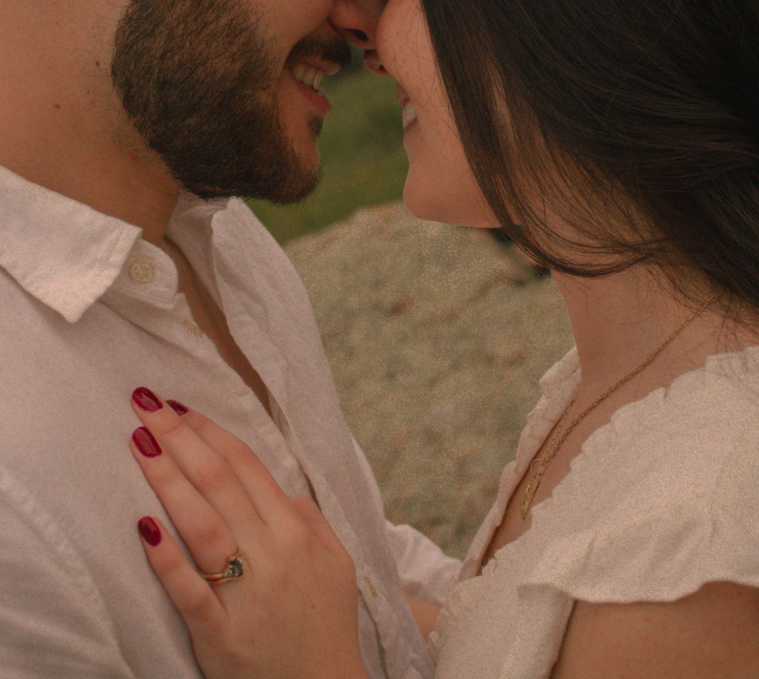 A close-up romantic moment between a couple in white clothing, with her red-painted nails visible.