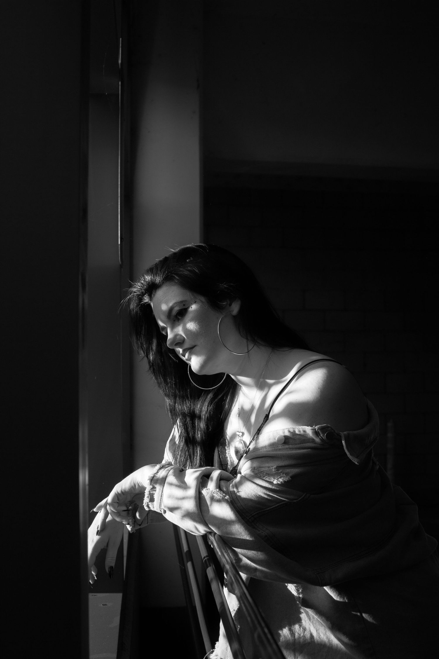 Dramatic black and white portrait with natural window light casting shadows on a figure in contemplative pose.