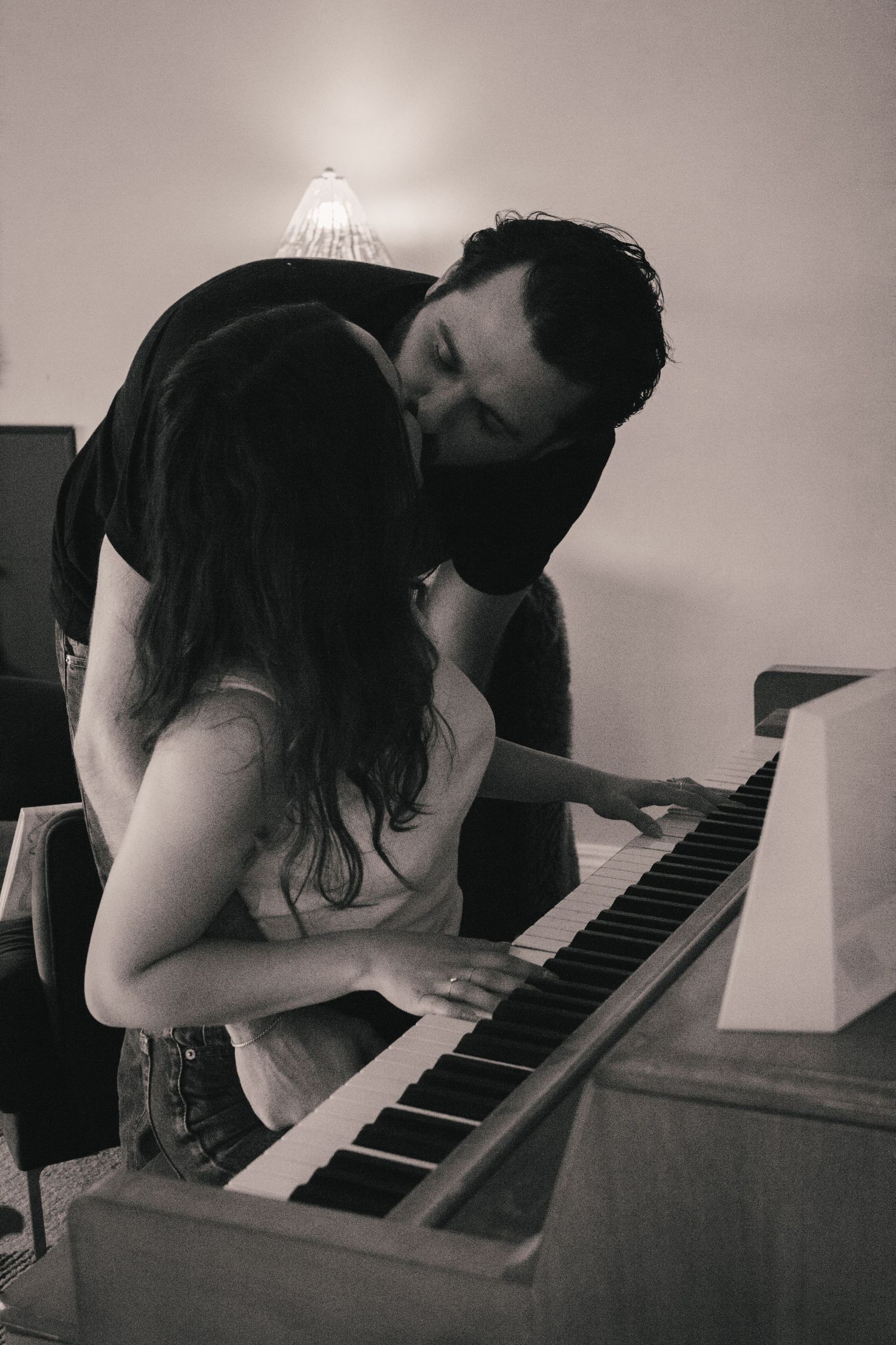 A couple shares an intimate moment at a piano in black and white photography.