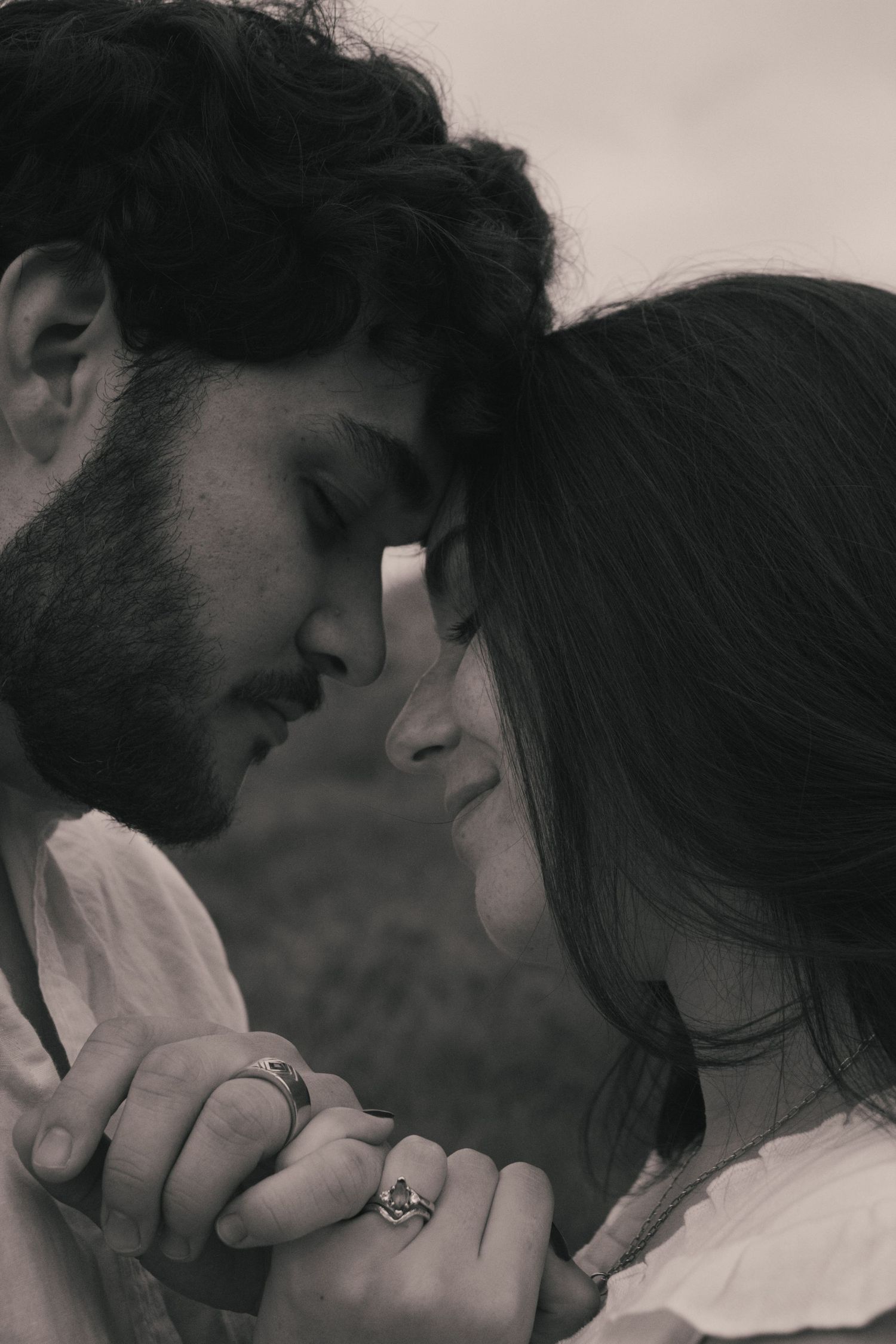 Intimate black and white portrait of a couple with clasped hands touching foreheads in a tender moment.