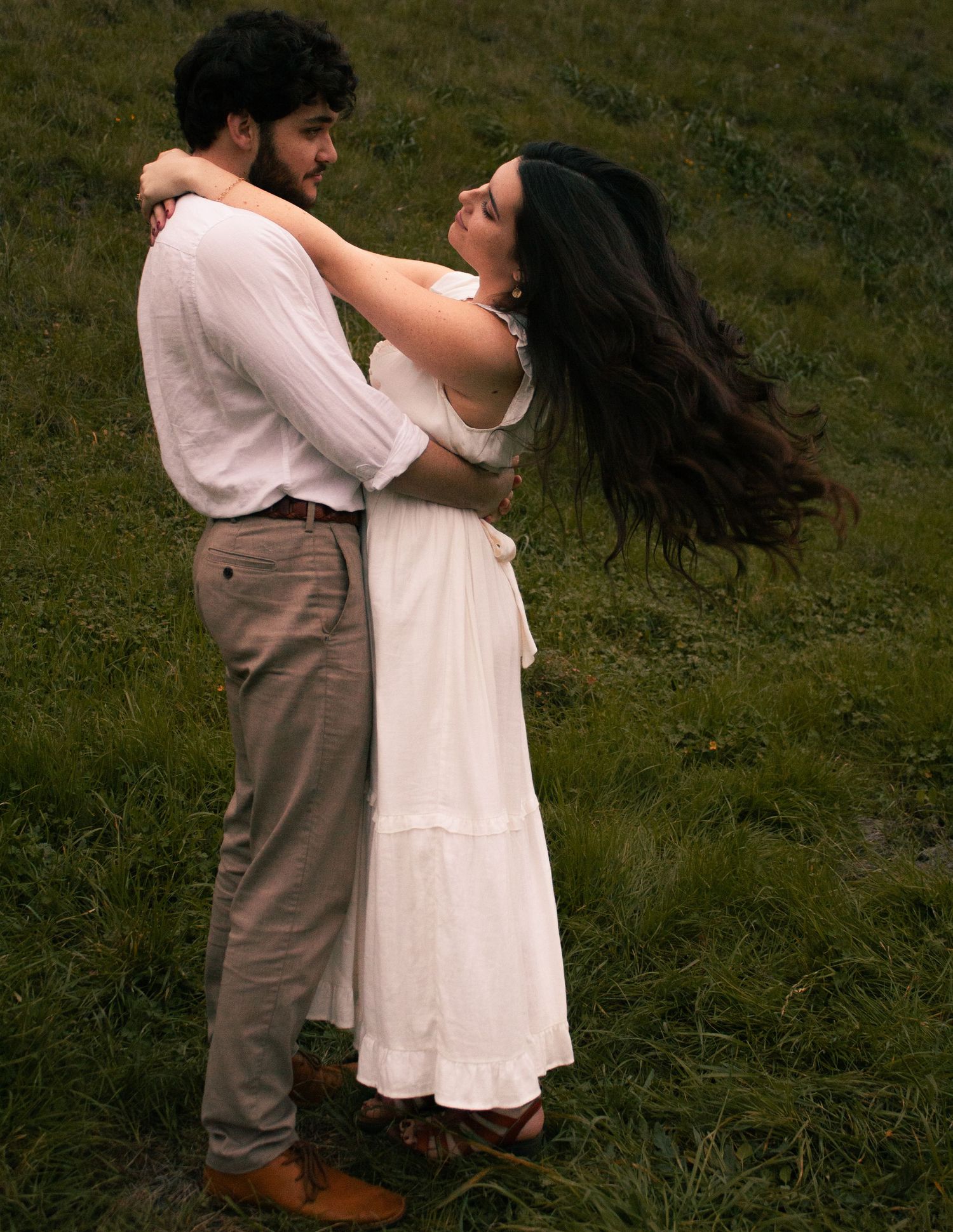 A couple shares an intimate embrace while dancing in a grassy field at dusk.