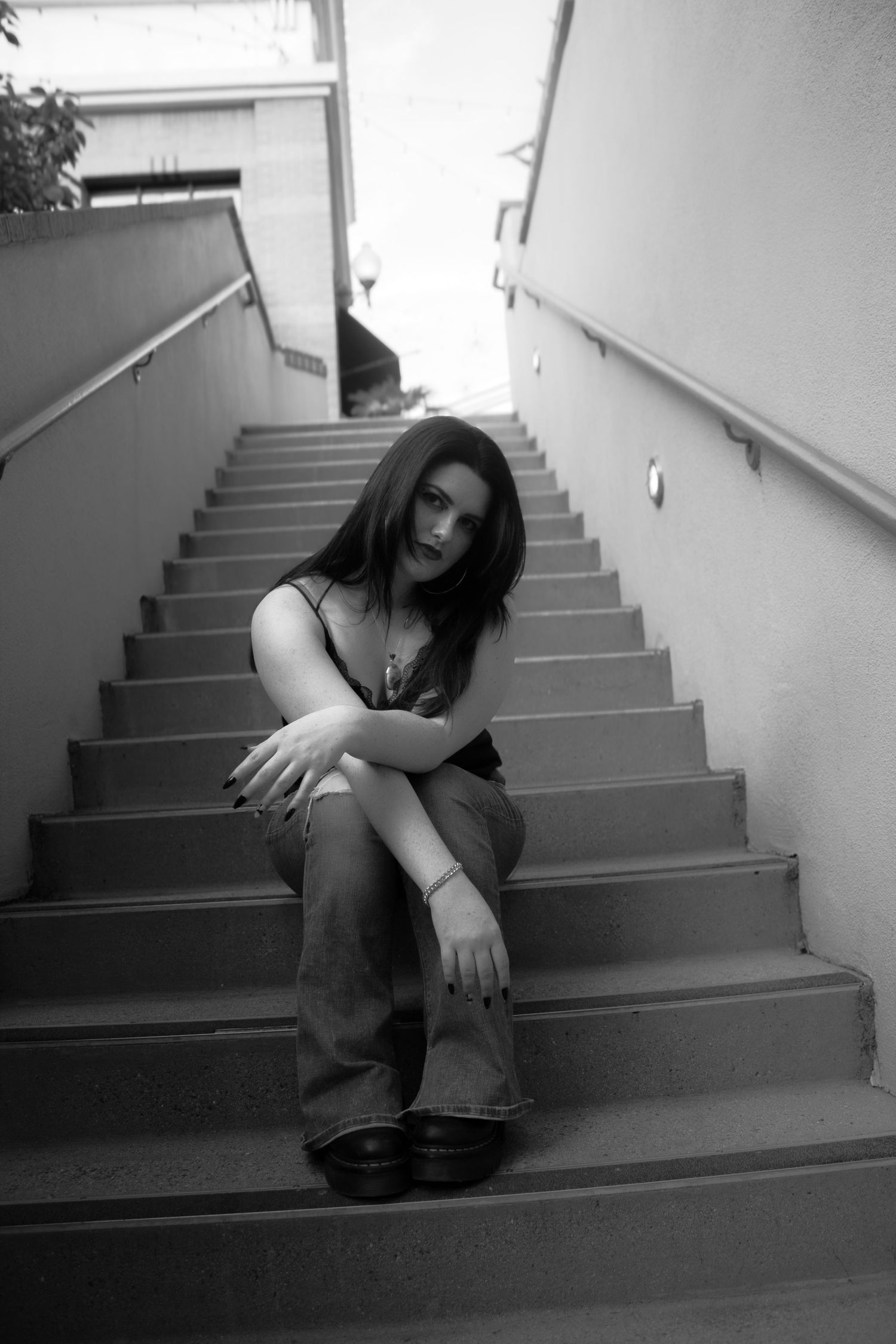 A black and white photograph of someone sitting alone on concrete stairs in a moody, contemplative pose.