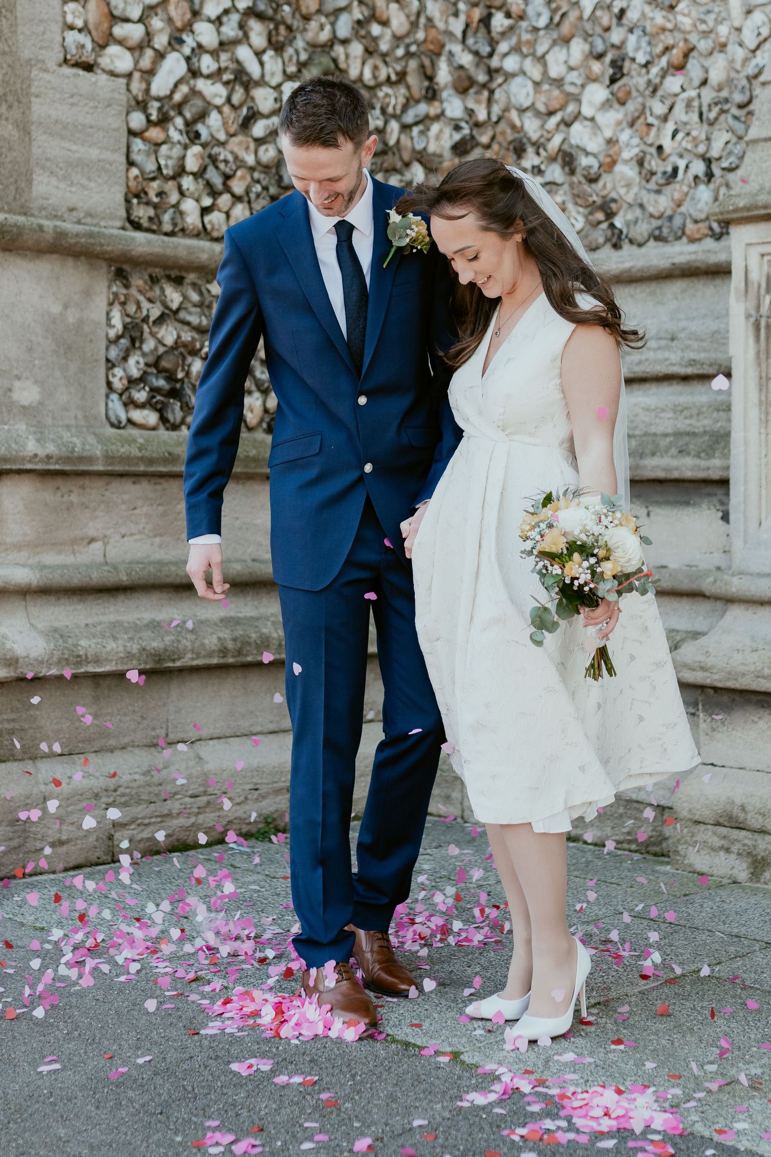 Pink flower petals scattered on stone steps as newlyweds stand together.