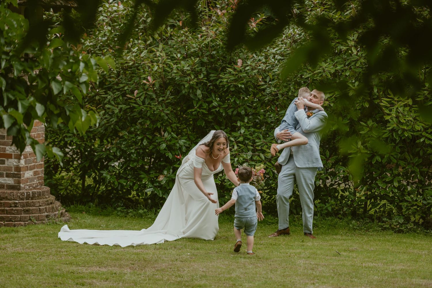 Wedding party playing with a small child on a grassy lawn.