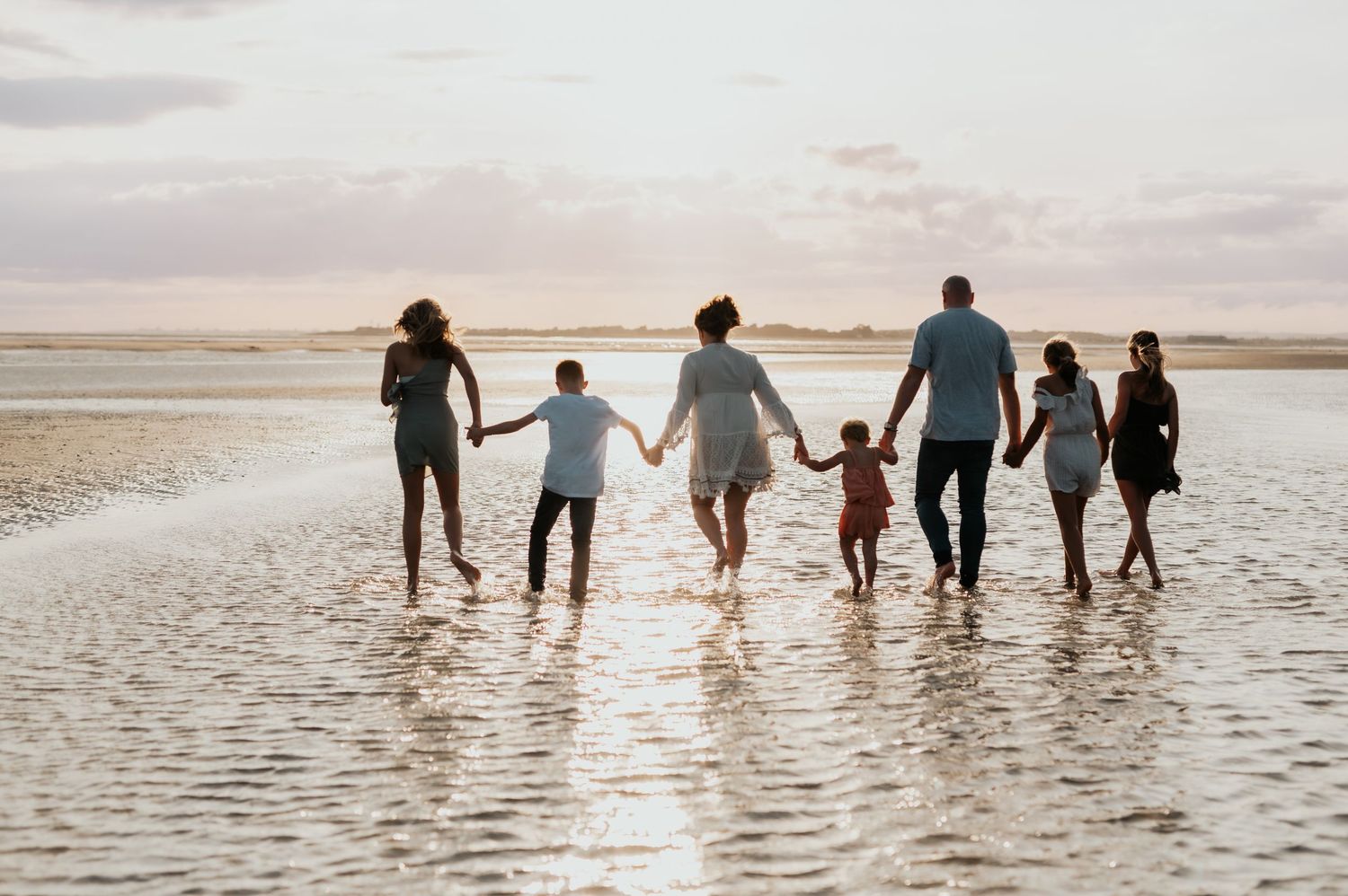 A group of people holding hands while walking along the shoreline at sunset on a beach.