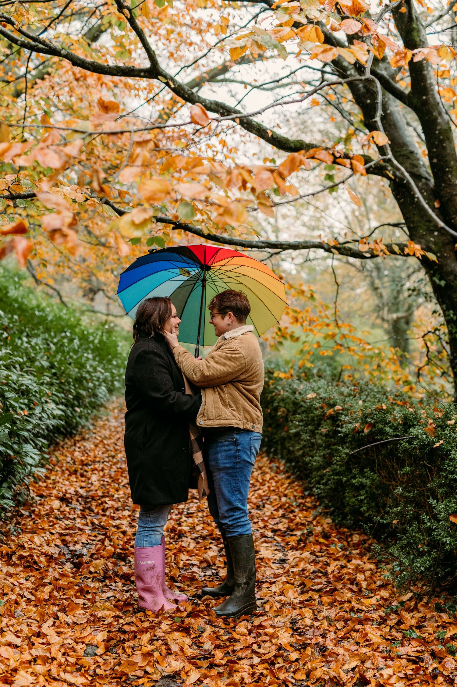 Two people sharing a moment under fall foliage with a rainbow umbrella.