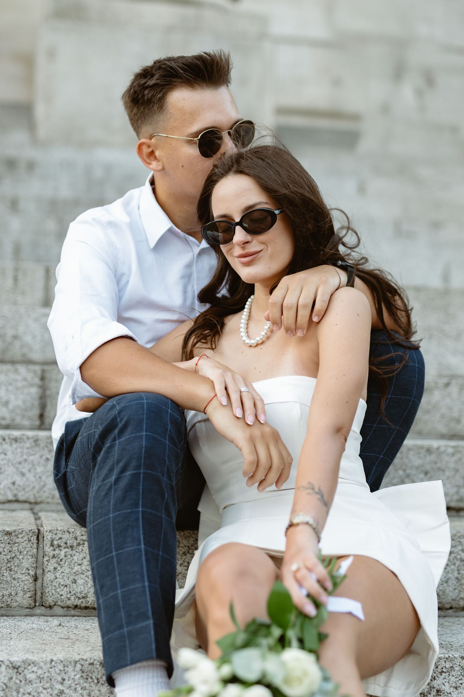 Intimate moments captured between couple on stone steps with white floral bouquet.