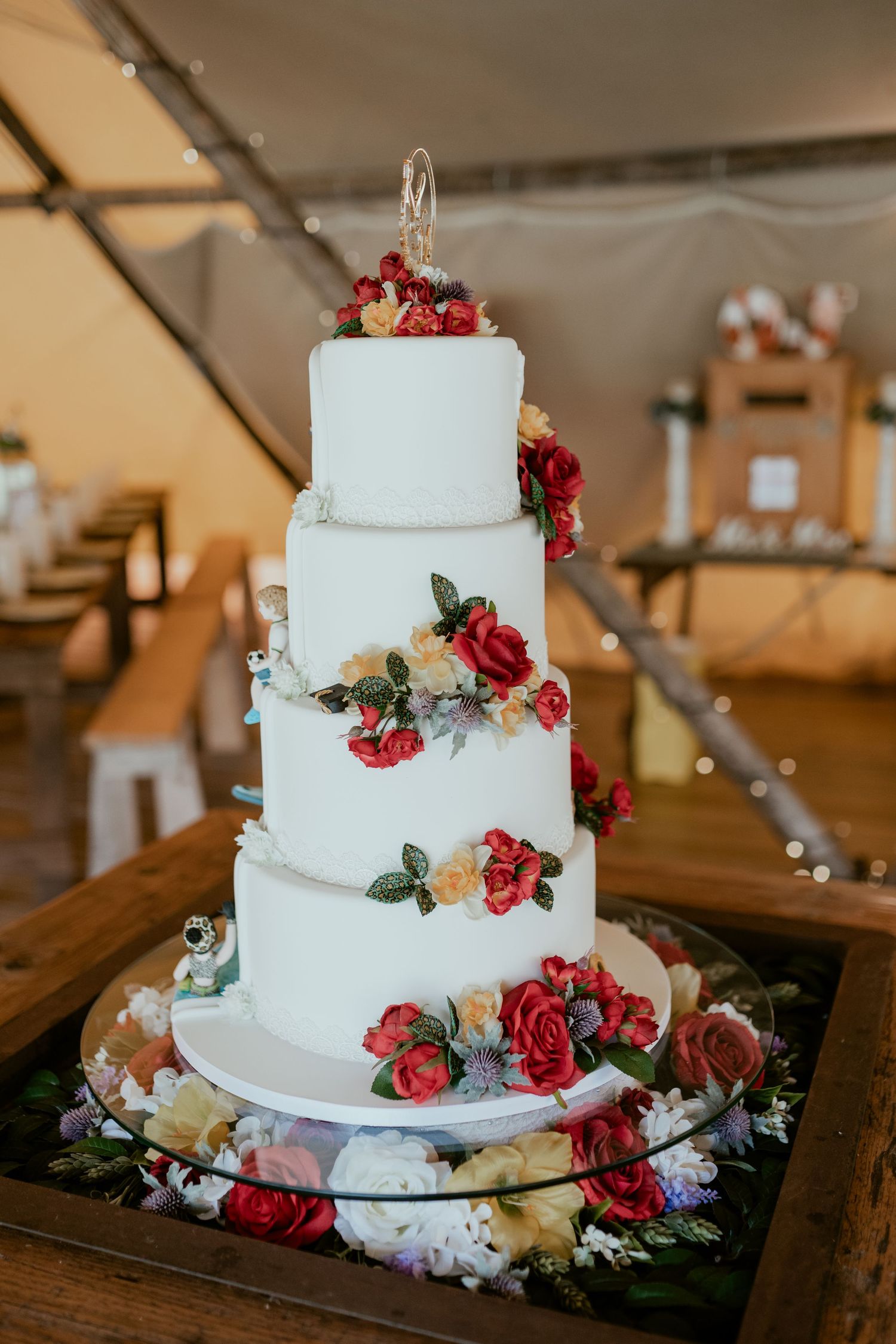 Four-tier white wedding cake decorated with cascading red roses and floral accents.