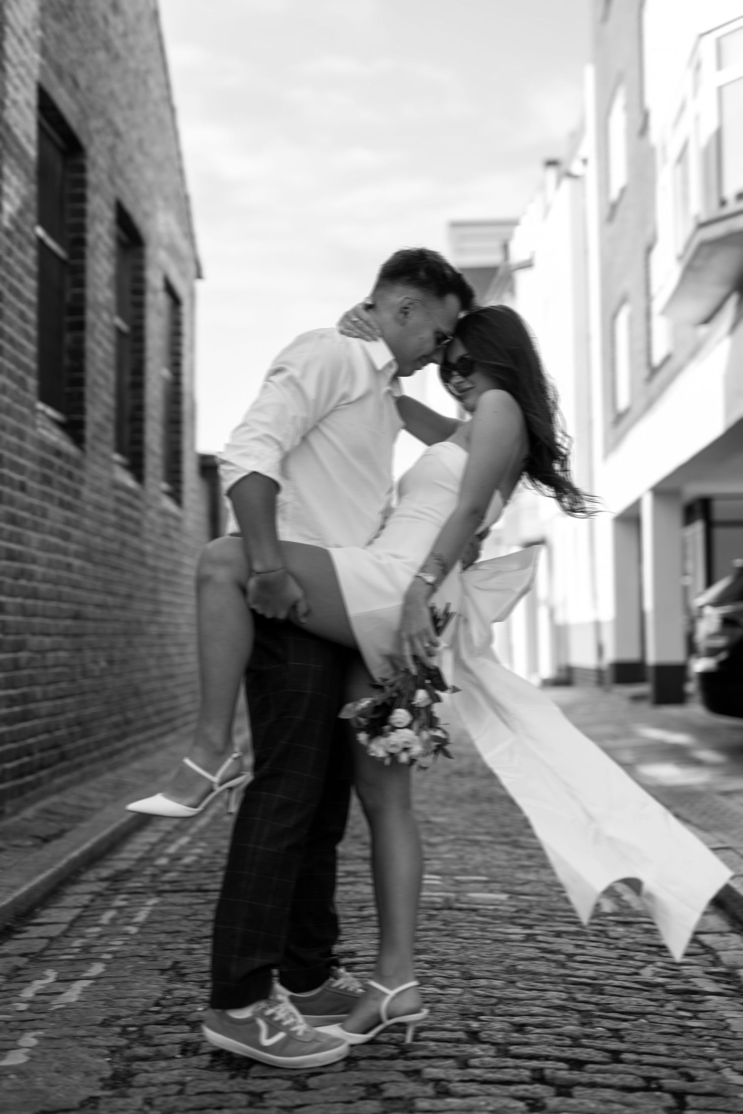 Romantic black and white photo of couple embracing on cobblestone street.