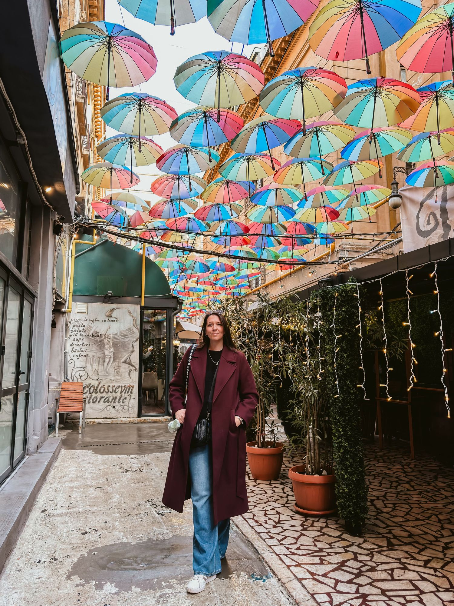 Colorful umbrellas create a vibrant canopy over a cobblestone street with string lights.