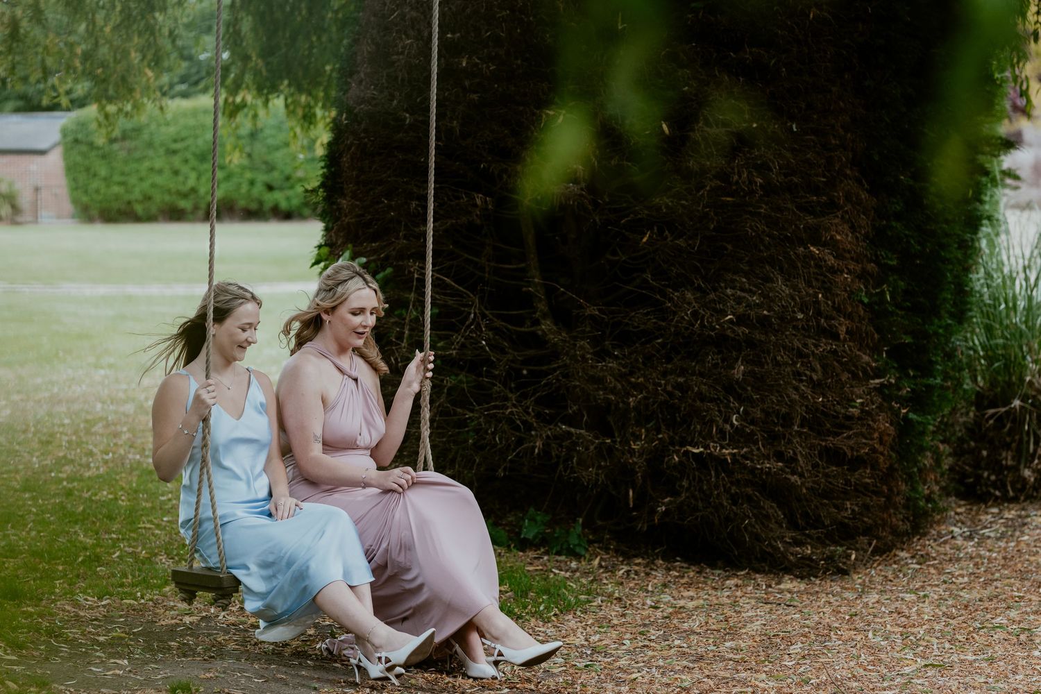 Bridesmaids in pastel dresses sitting together on outdoor swings.