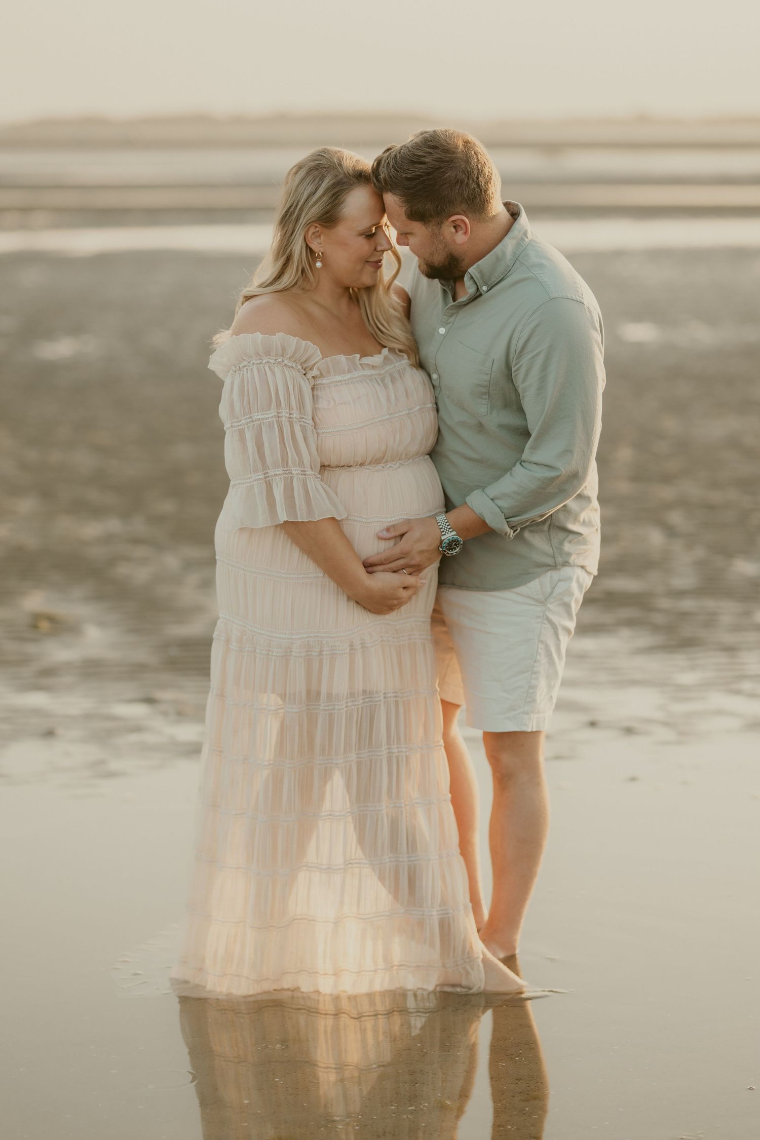 Romantic maternity beach photos at sunset with soft pastel colors.