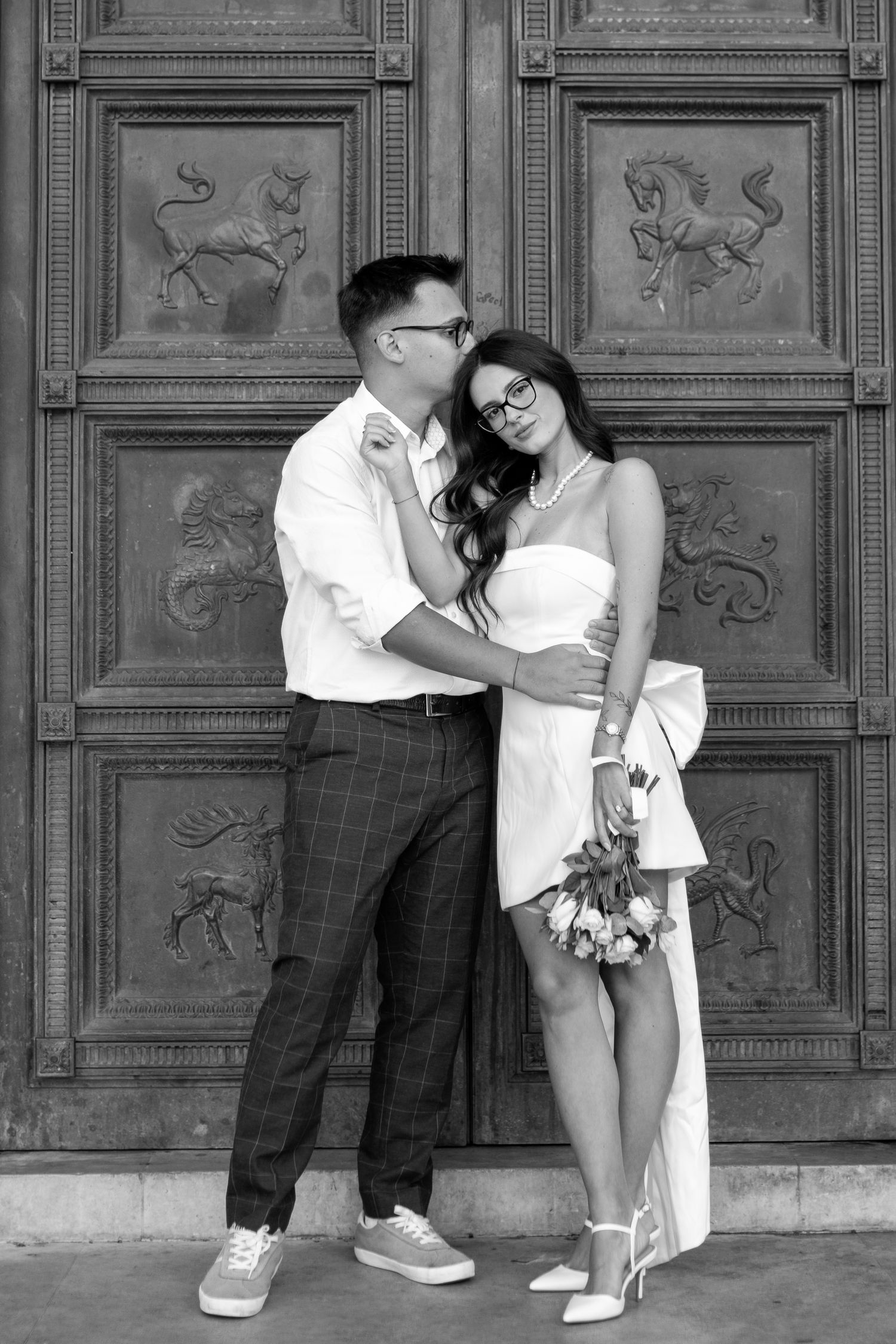 Couple posing playfully against ornate wooden panels in black and white.